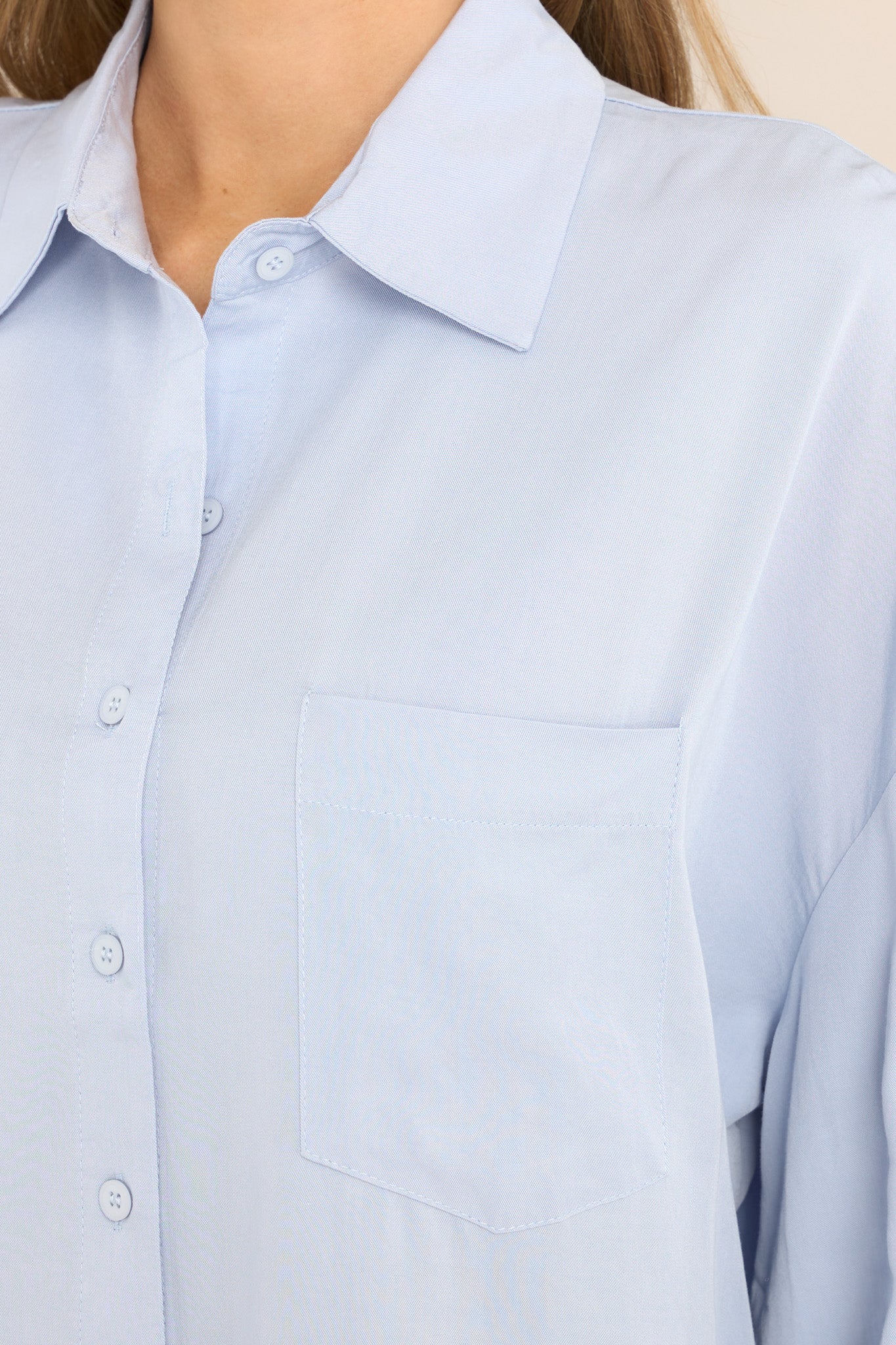 Close-up of the collared neckline, functional buttons, chest pocket, and button cuffed long sleeves of a light blue top.