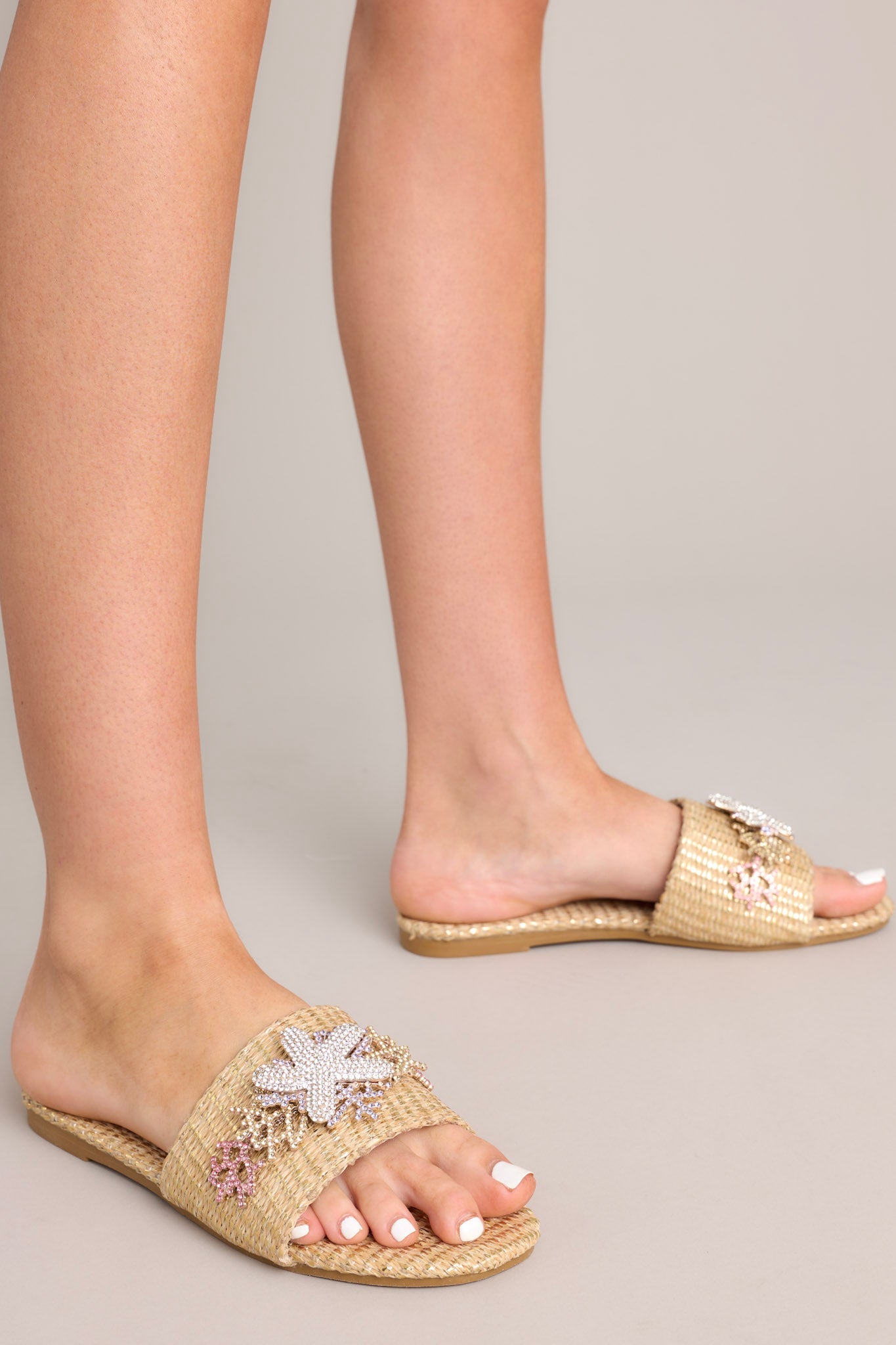 Side view of these sandals that feature a rounded toe, a slip-on design, a wicker-like material, and tropical multicolored rhinestone detailing.