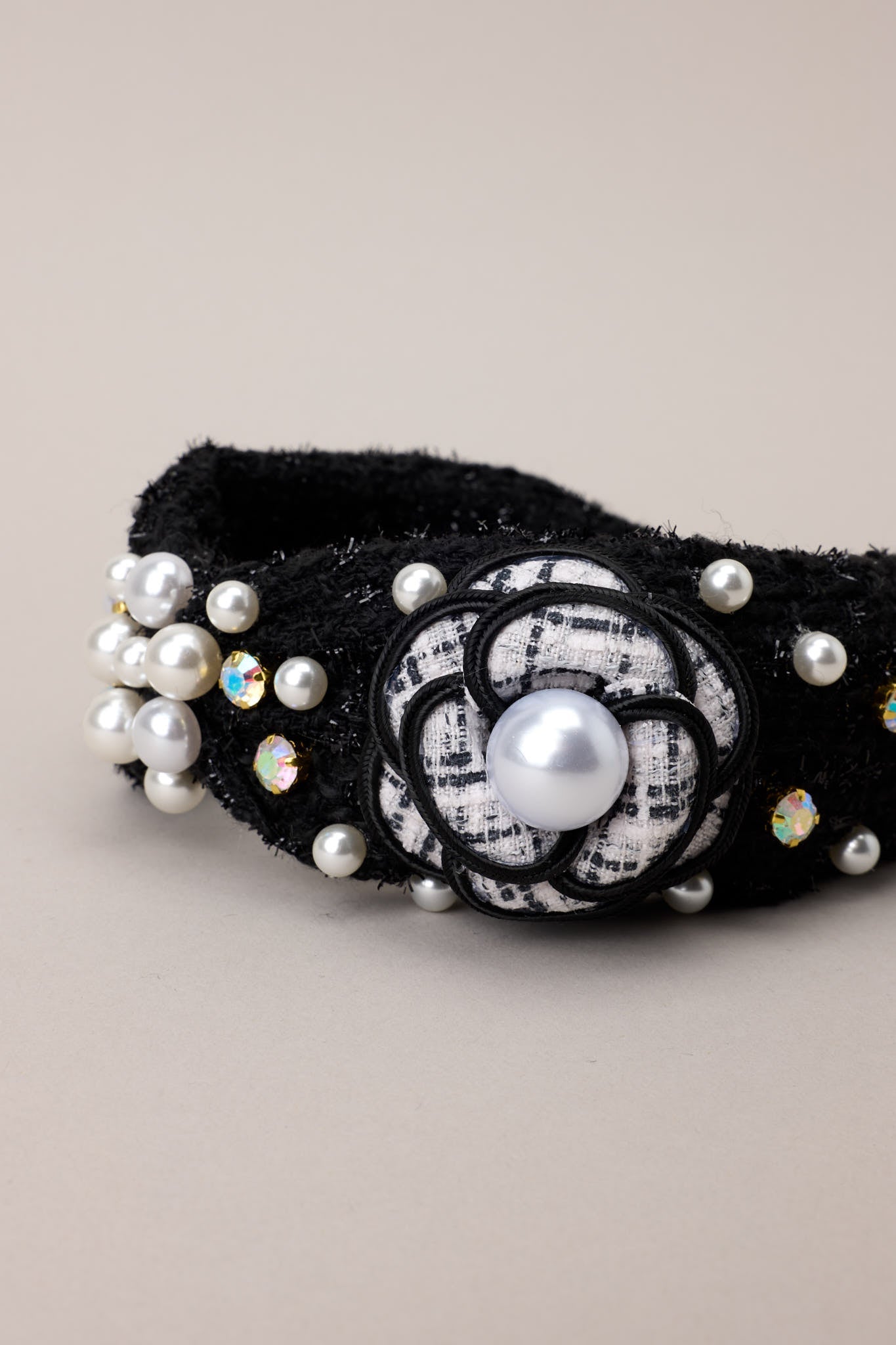 "Focused view of the headband’s black and white tweed flower, surrounded by pearl and rhinestone accents.