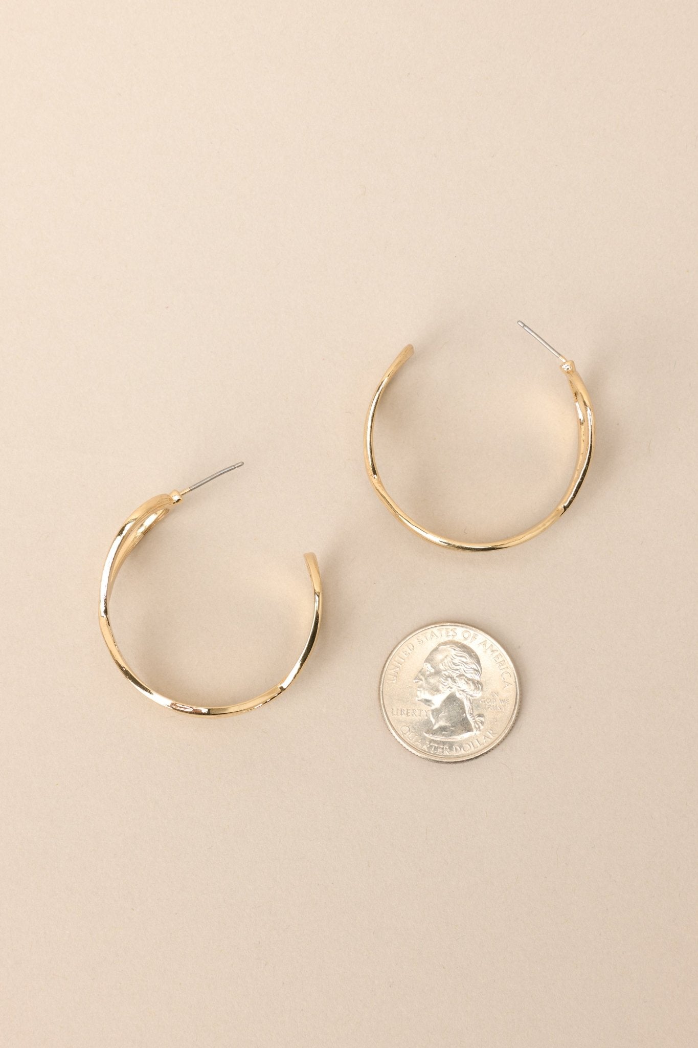 Size comparison of these gold hoop earrings that feature gold hardware, a textured and twisted design, and secure post backings.