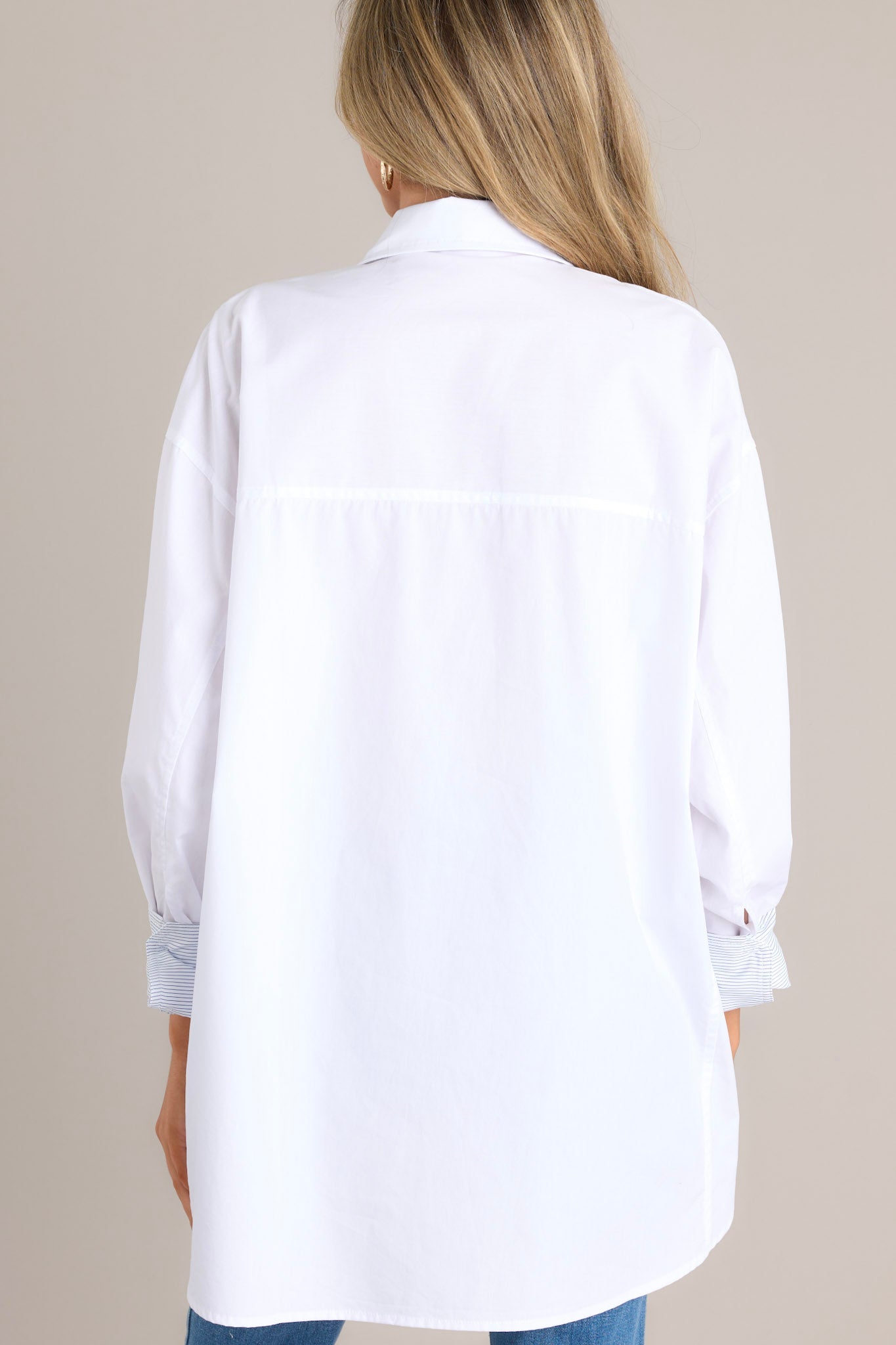 Back view of a white top highlighting the striped button cuff sleeves, split scoop hemline, and overall fit.