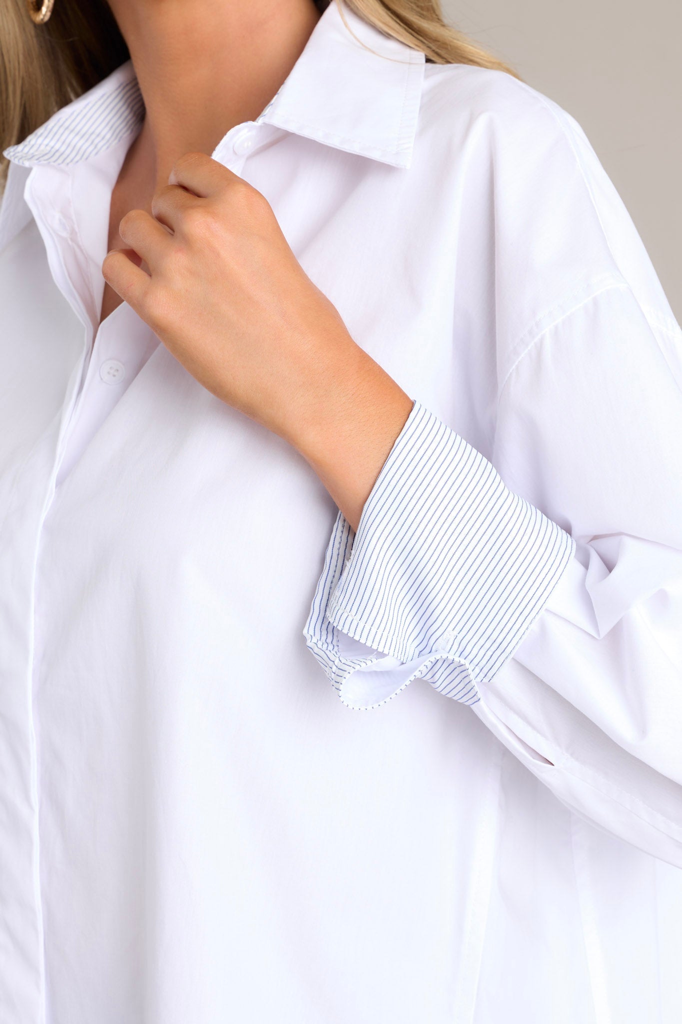 Close-up of the white top showing the collared neckline, full button front, and striped button cuff sleeves.