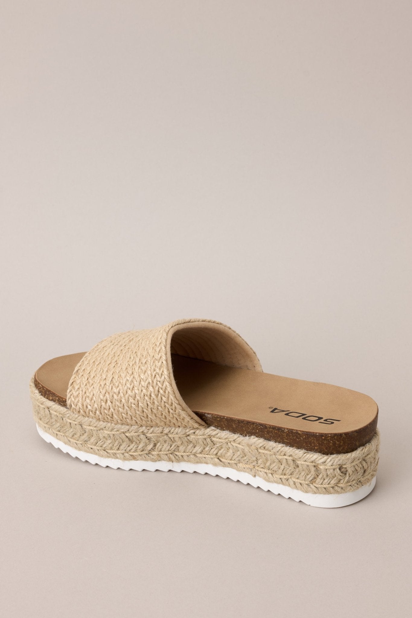 Angled back view of these natural sandals with rounded toe, slip-on design, strap over foot, espadrille detailing, textured sole.