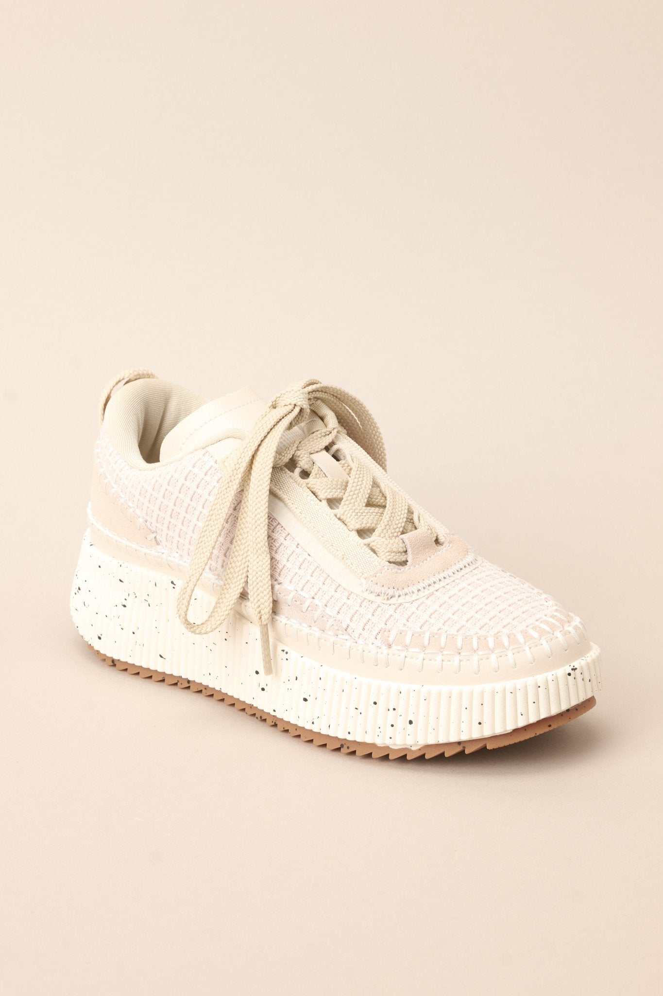 Angled front view of these  beige sneakers with rounded toe, functional laces, knitted detailing, comfortable fit, thick speckled sole.