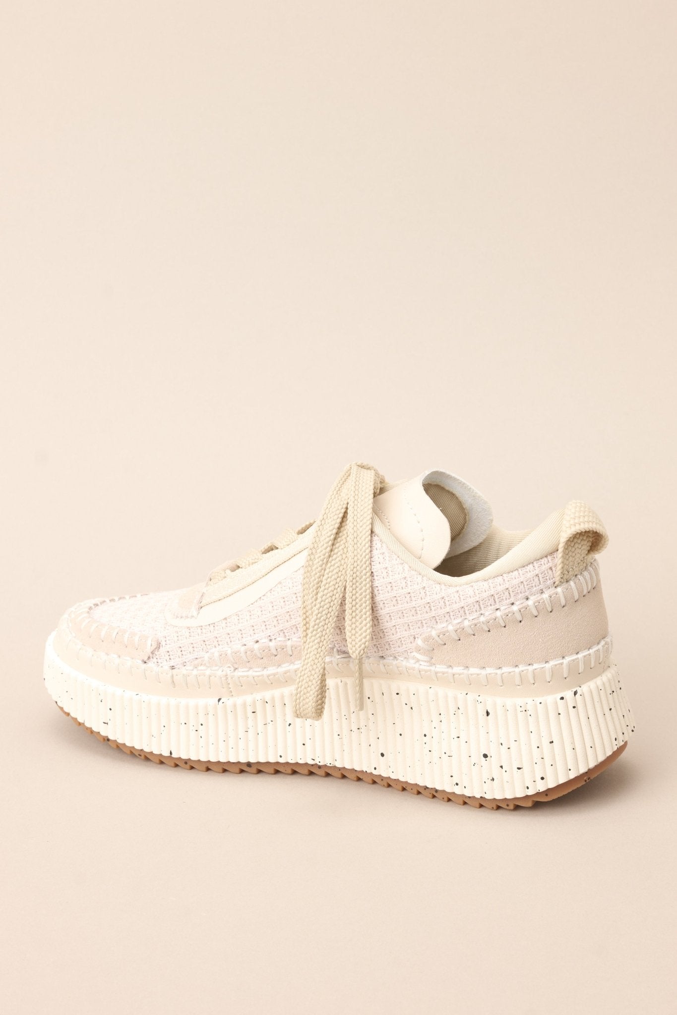 Angled back view of these beige sneakers with rounded toe, functional laces, knitted detailing, comfortable fit, thick speckled sole.