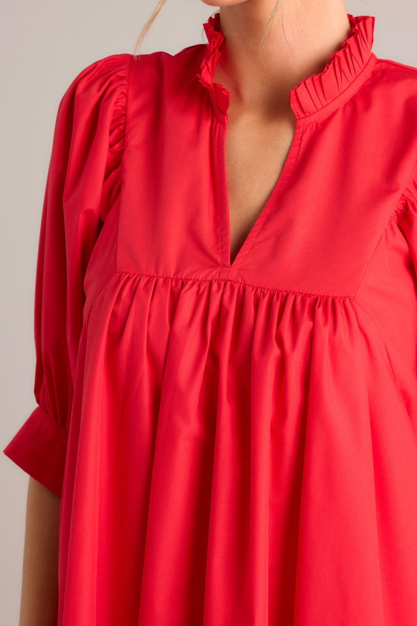 Close up view of the neckline of this red mini dress that features a v-neckline, a ruffled faux collar, pleated detailing around the bust, functional hip pockets, and cuffed puff sleeves.