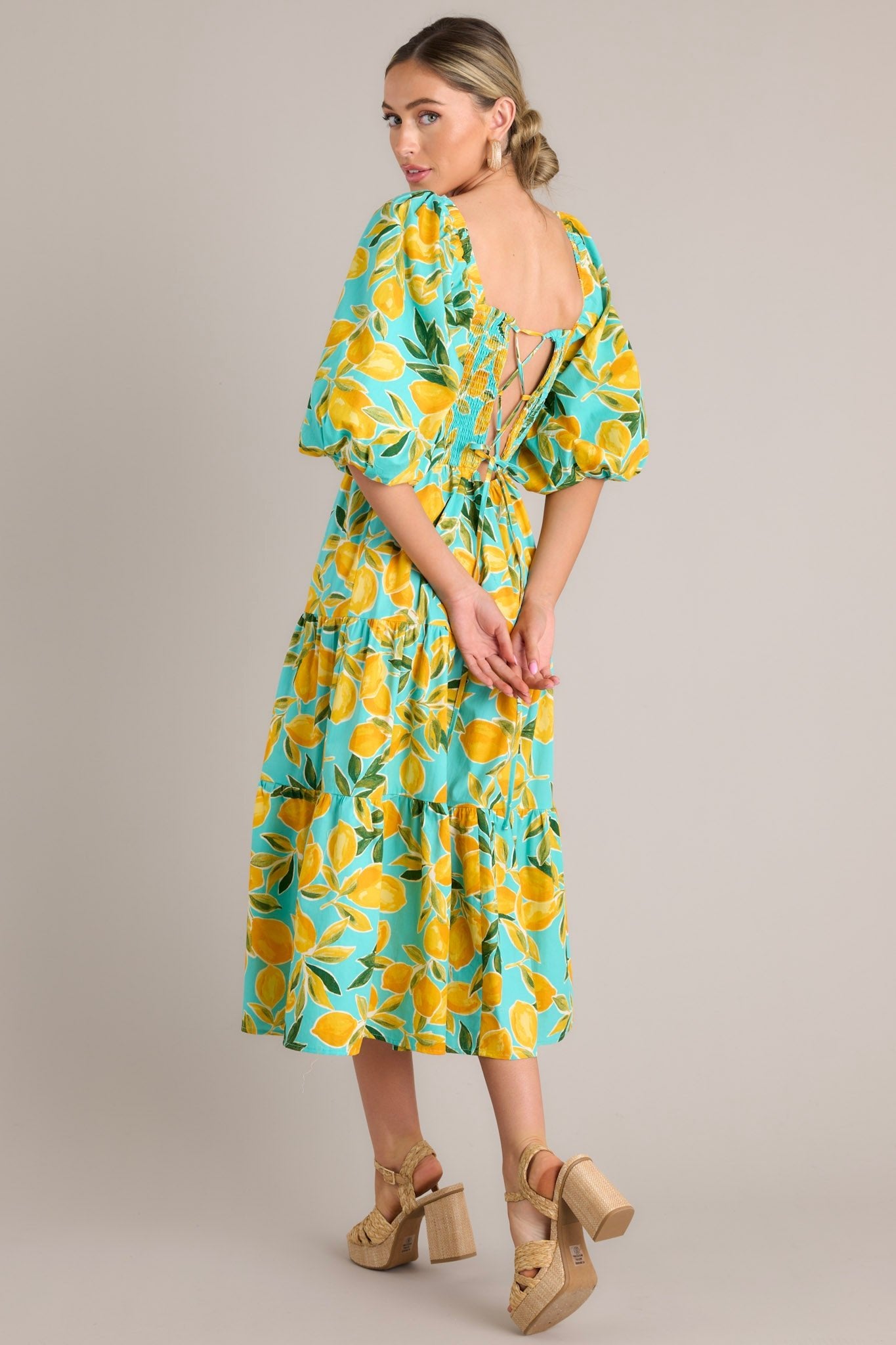 An angled back view of the dress, focusing on the corset-style lacing, flowing tiered skirt, and vibrant lemon pattern against the aqua fabric.