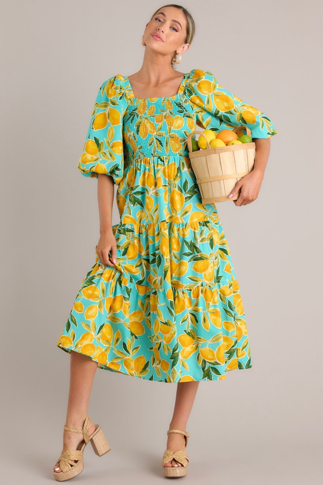 A vibrant aqua dress with a smocked bust, puff sleeves, and a tiered skirt, showcasing a lemon print in a full front view.