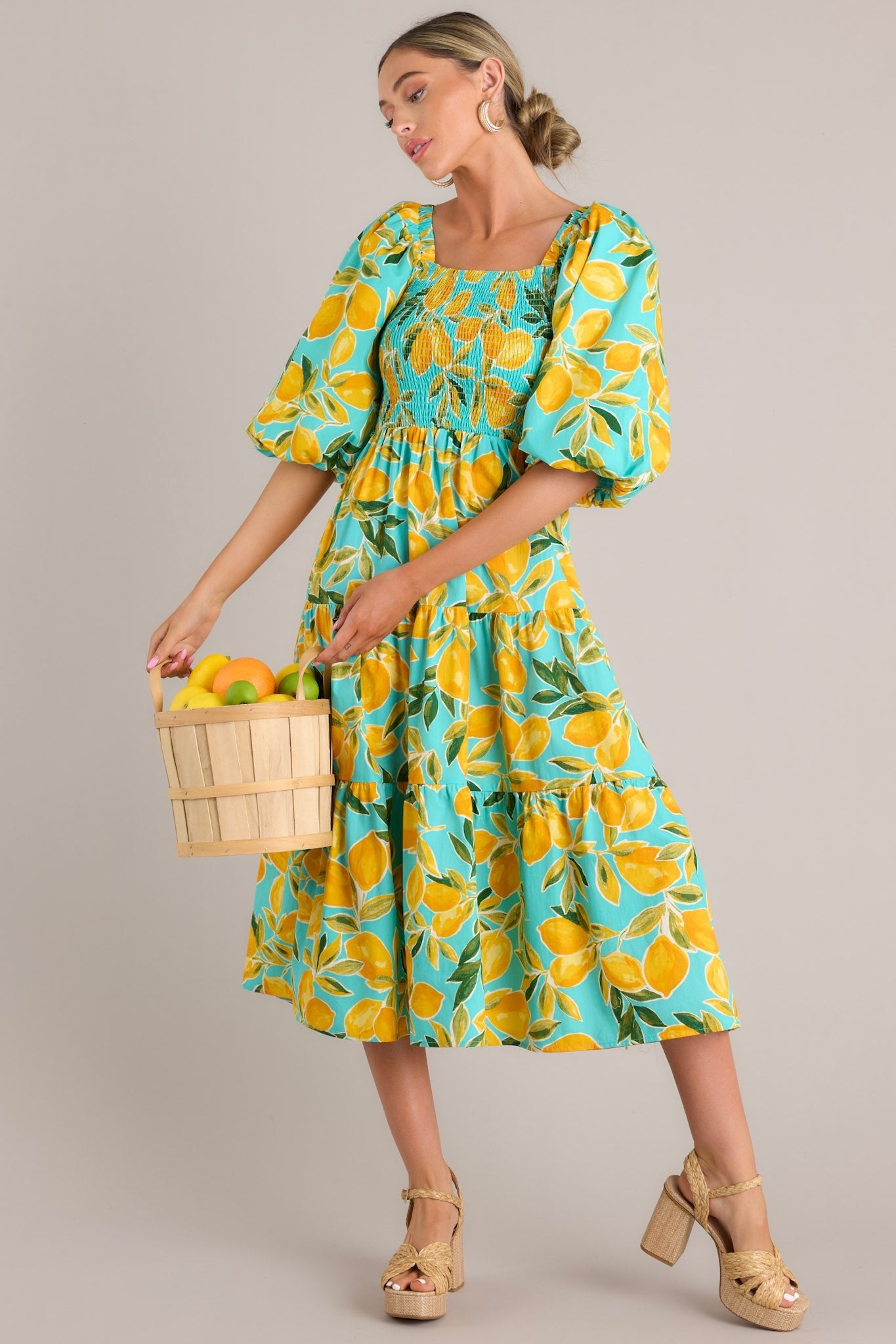 An angled view of the dress, highlighting the smocked bodice, puff sleeves, and flowy tiered skirt with its aqua lemon pattern.