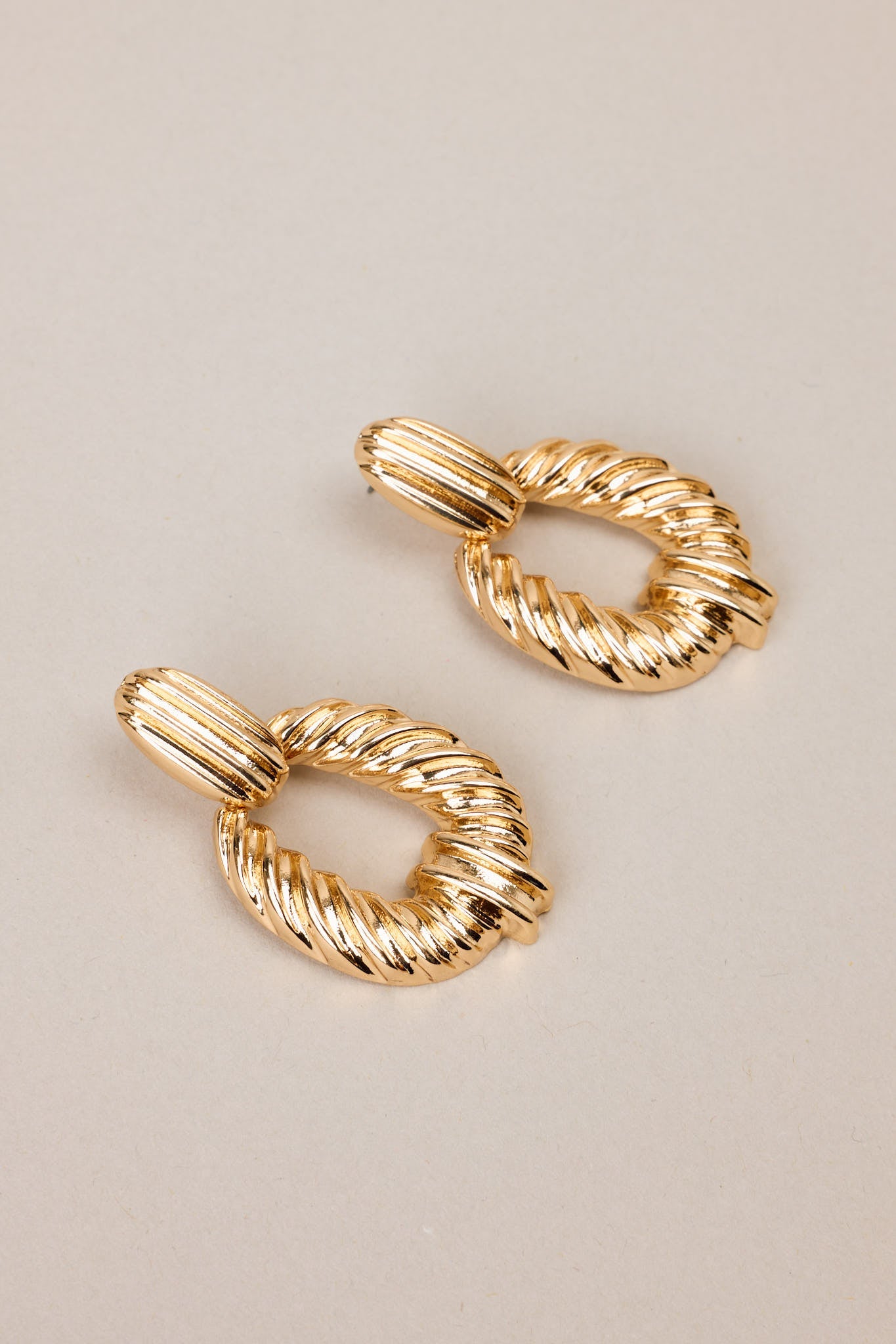 Angled overhead view of these gold earrings with rectangular-shaped studs, textured dangles, secure post backings.