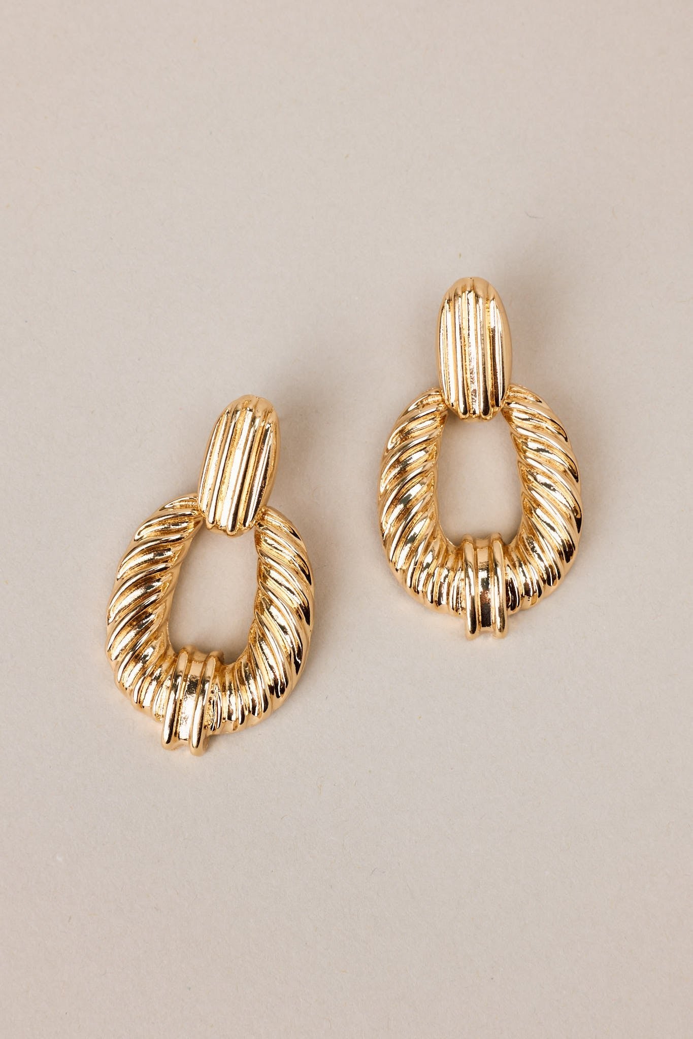 Overhead view of these gold earrings with rectangular-shaped studs, textured dangles, secure post backings.