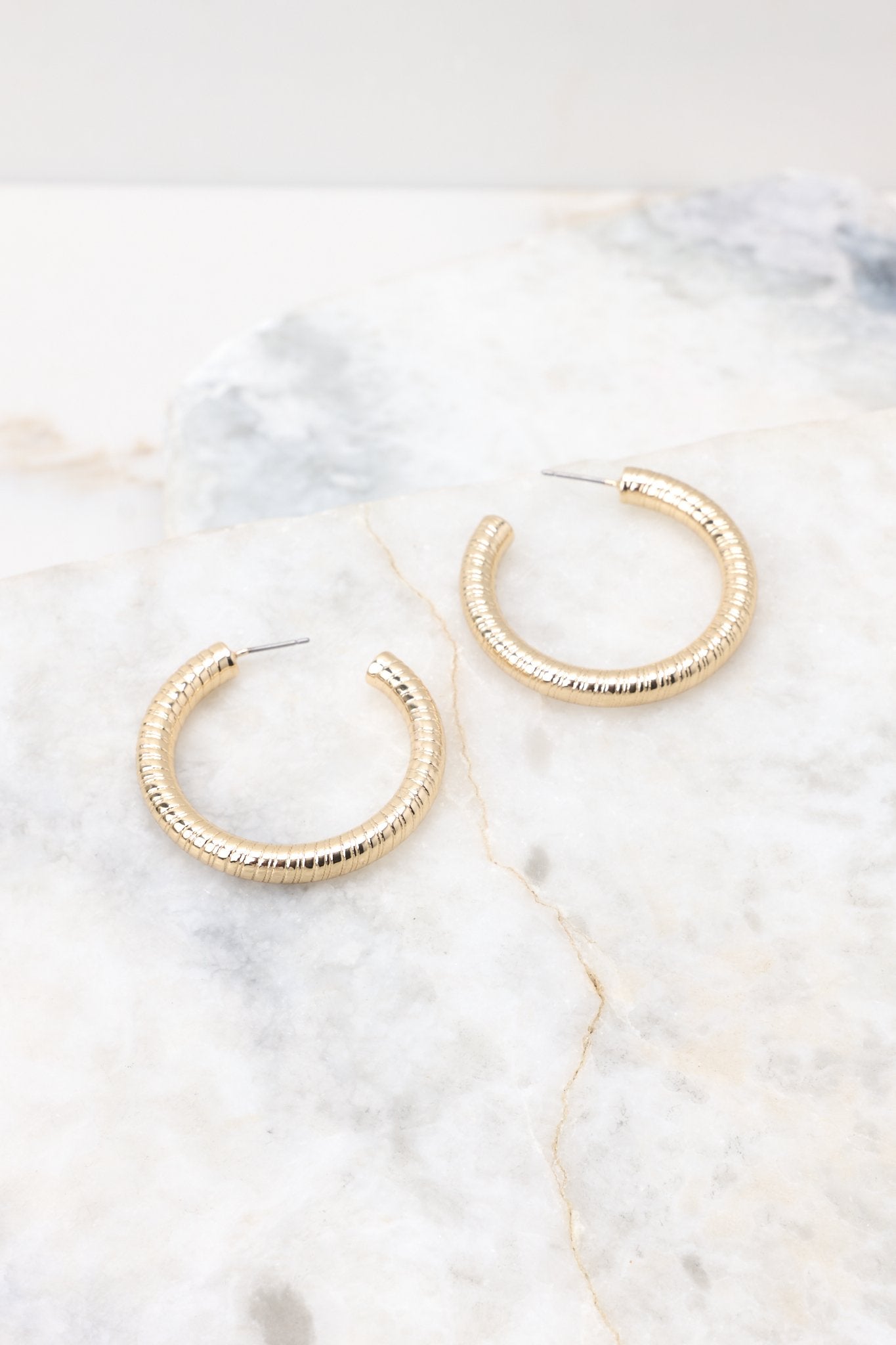 Angled overhead view of these gold hoop earrings that feature a textured gold finish, and a secure post-back fastening.