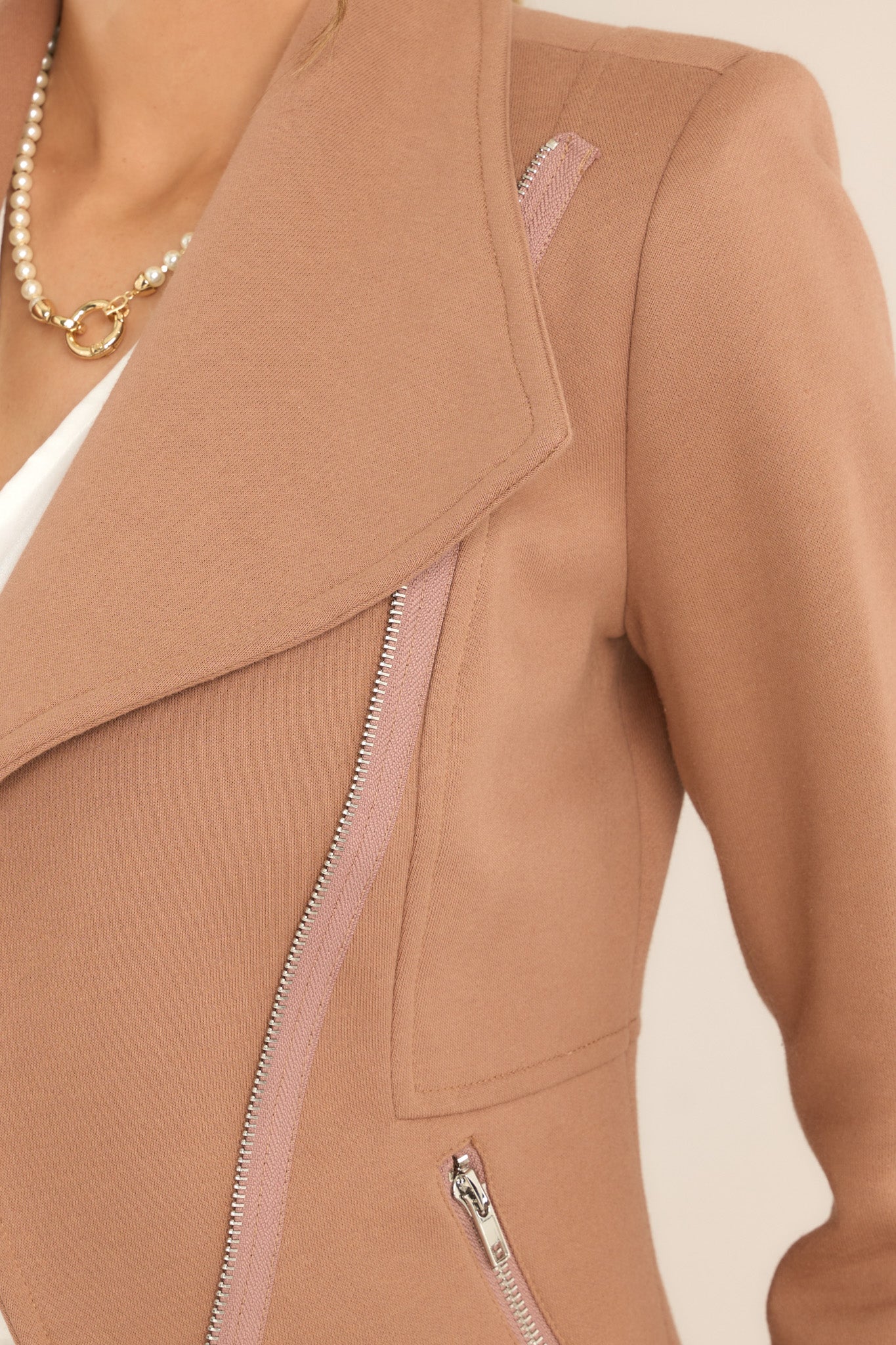 Close-up of the shoulder pads, cross zipper closure, functional waist pockets with zipper closure, lapels, and silver hardware of a mocha tan moto jacket.