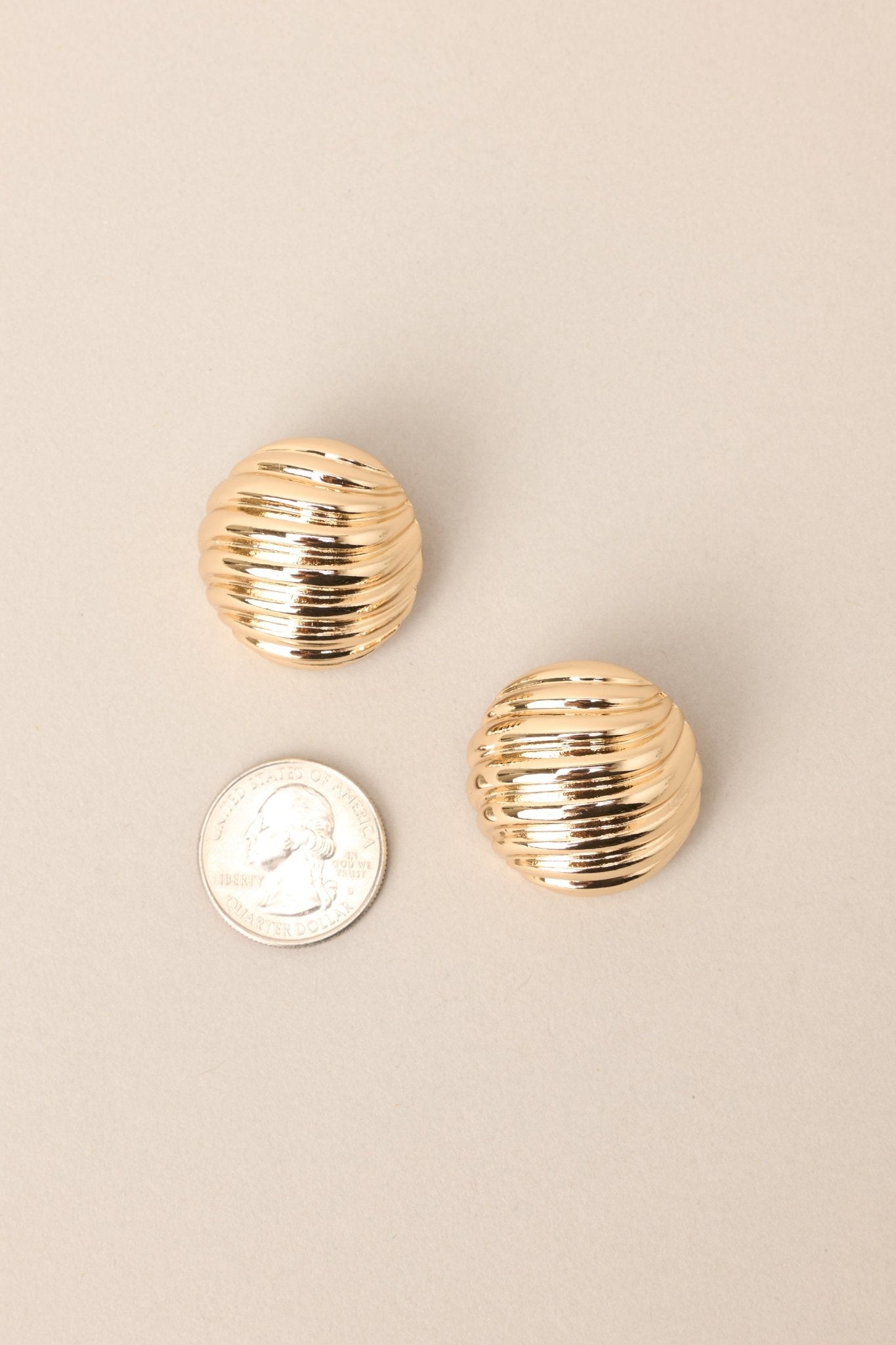 Size comparison of these view of these gold earrings with circular shape, wave-like texture, secure post backing