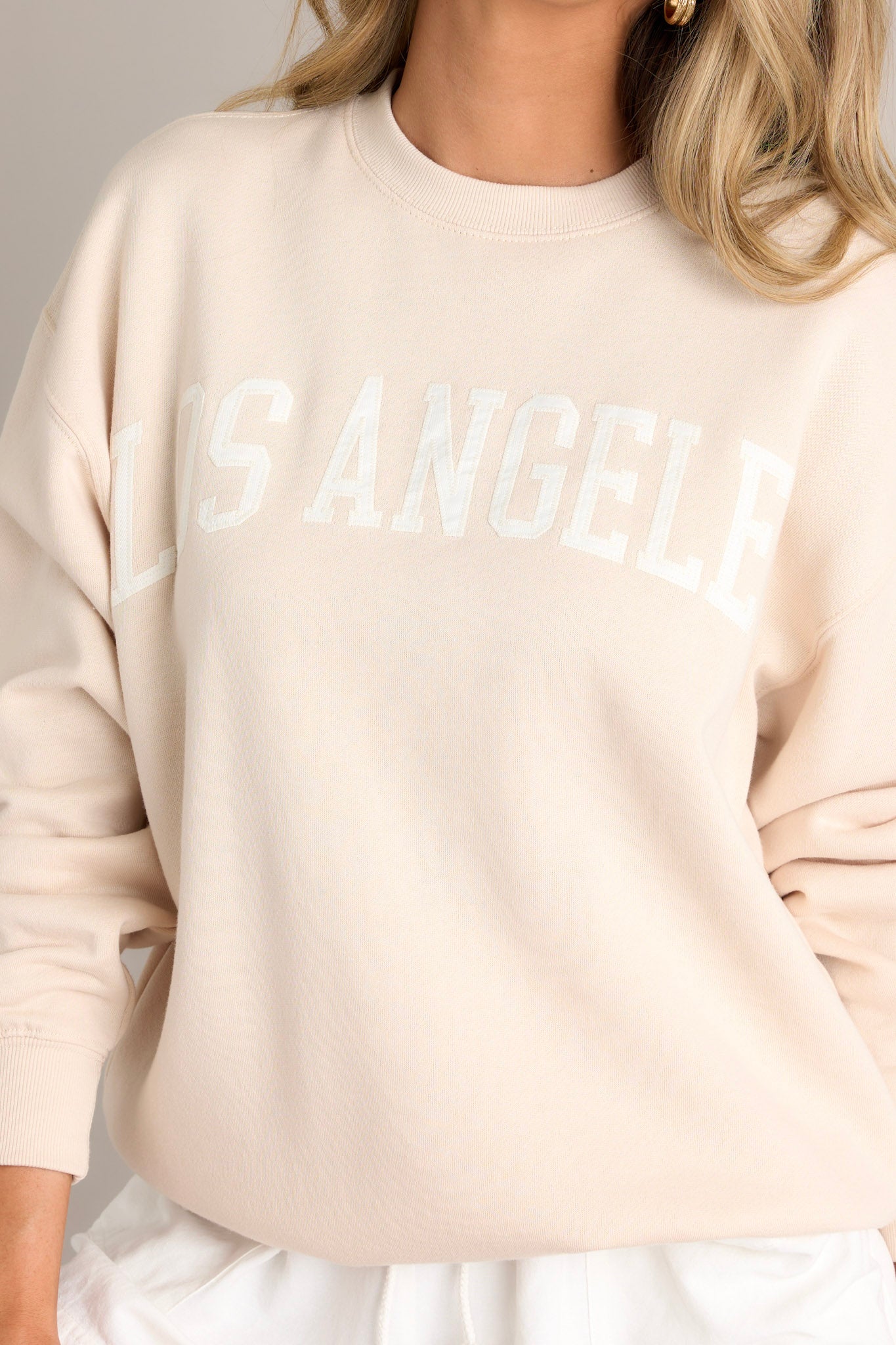 Close up view of this natural embroidered sweatshirt that features "Los Angeles" across the bust, a crew neckline, and ribbed hems.