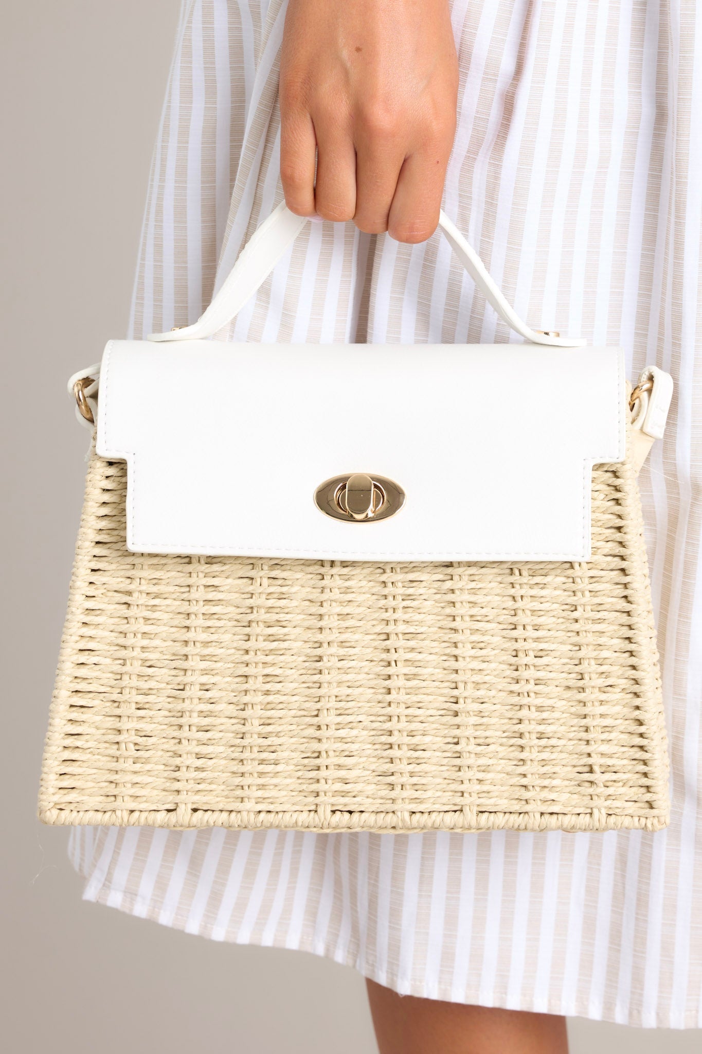 This woven handbag features gold hardware, a thick top handle, faux leather, a twist lock closure, a zipper pocket inside and an adjustable shoulder strap.