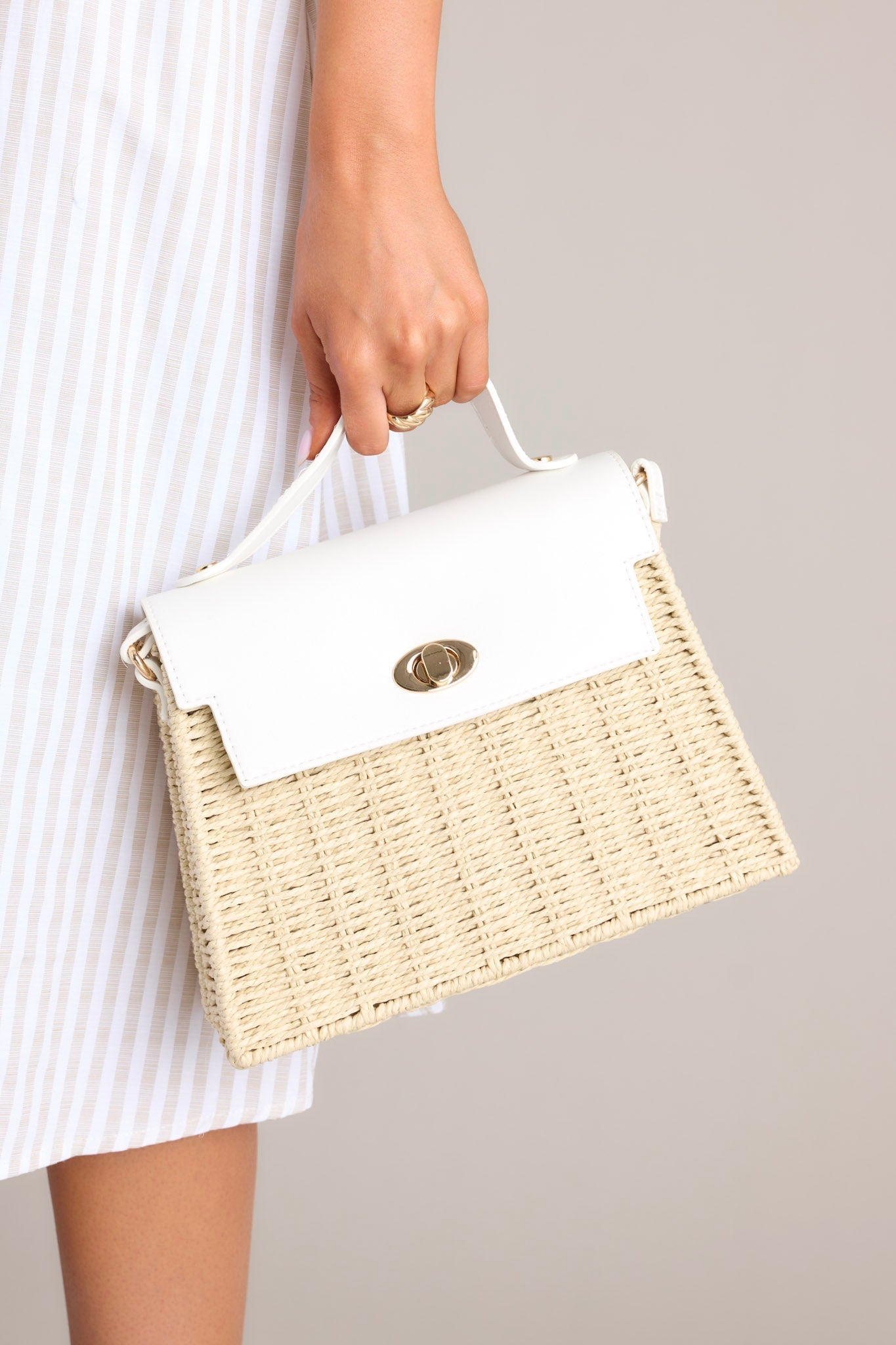 Close-up angled view of this woven handbag that features gold hardware, a thick top handle, faux leather, a twist lock closure, a zipper pocket inside and an adjustable shoulder strap.