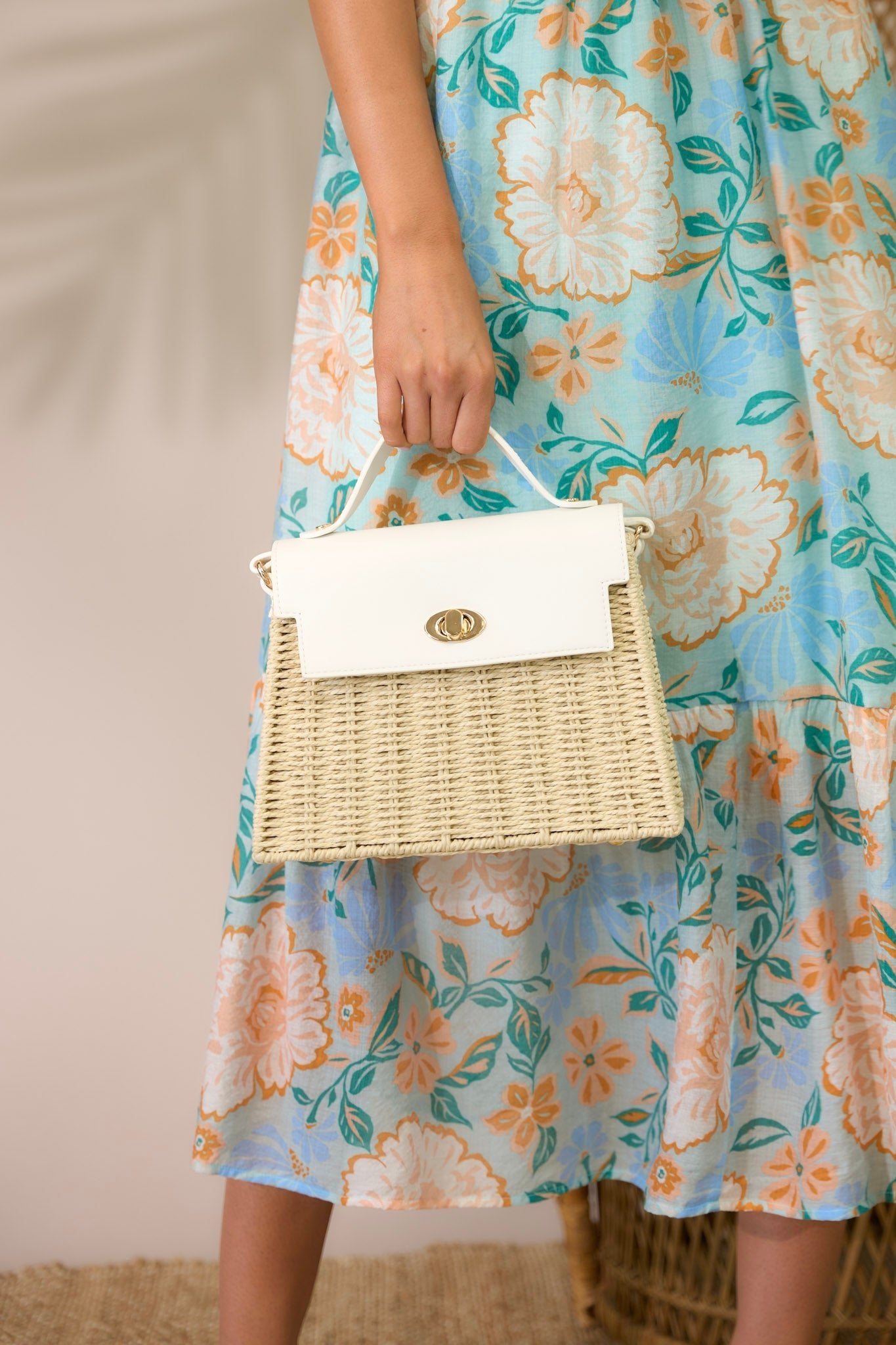 Angled front view of this woven handbag that features gold hardware, a thick top handle, faux leather, a twist lock closure, a zipper pocket inside and an adjustable shoulder strap.