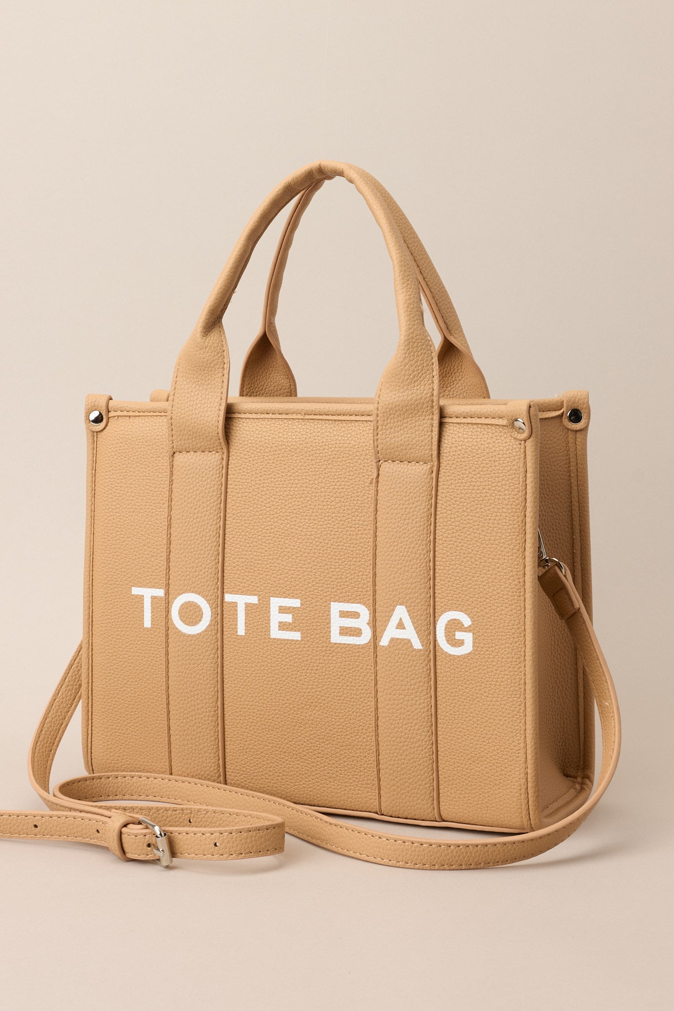 Angled front view of this tan bag that features silver hardware, top handles, a functional zipper closure, an additional pocket on the inside, and a removable strap.