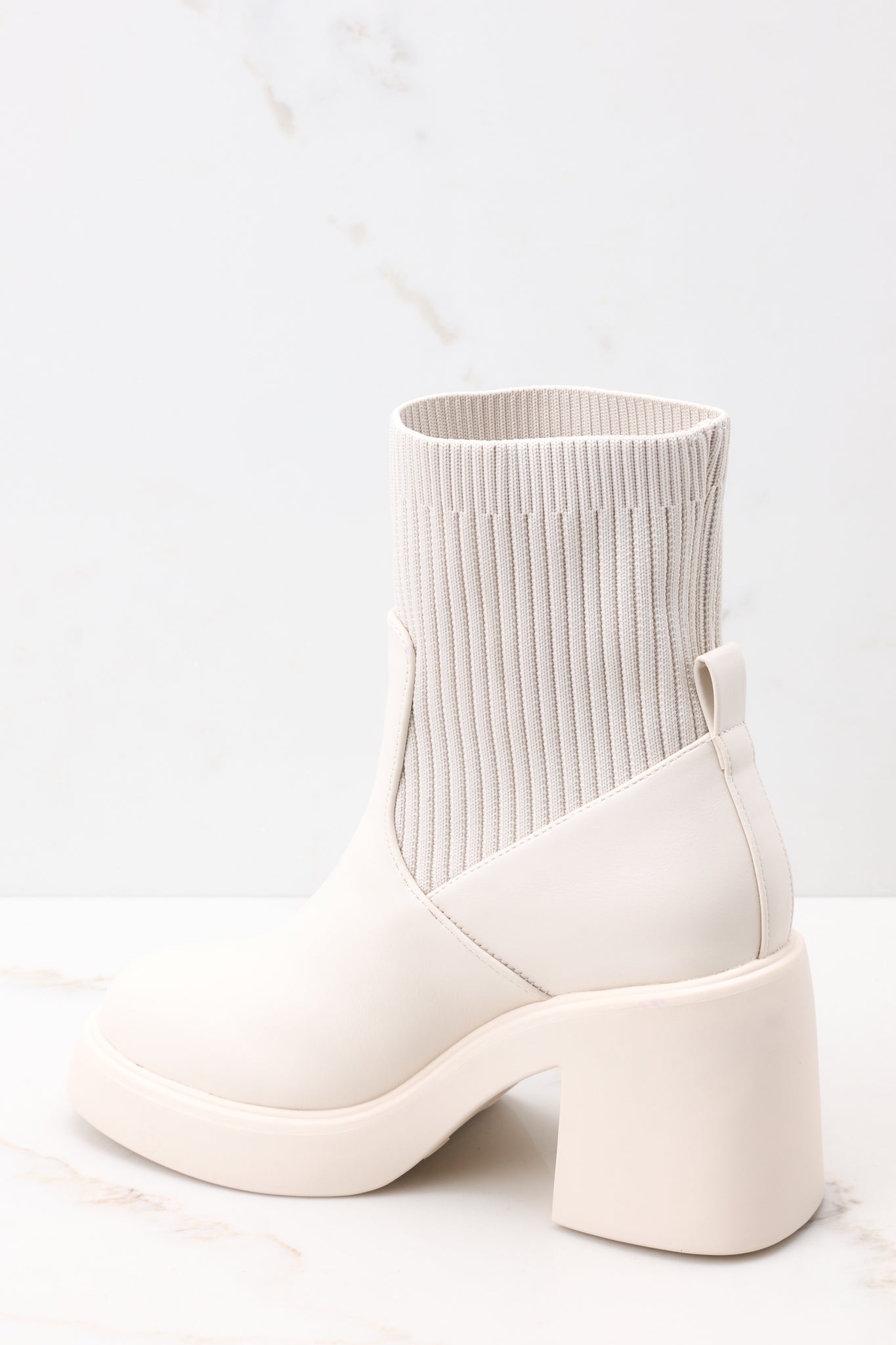 Back angled view of these boots featuring a rounded toe, a platform heel, and a stretchy ribbed cloth material around the ankle.