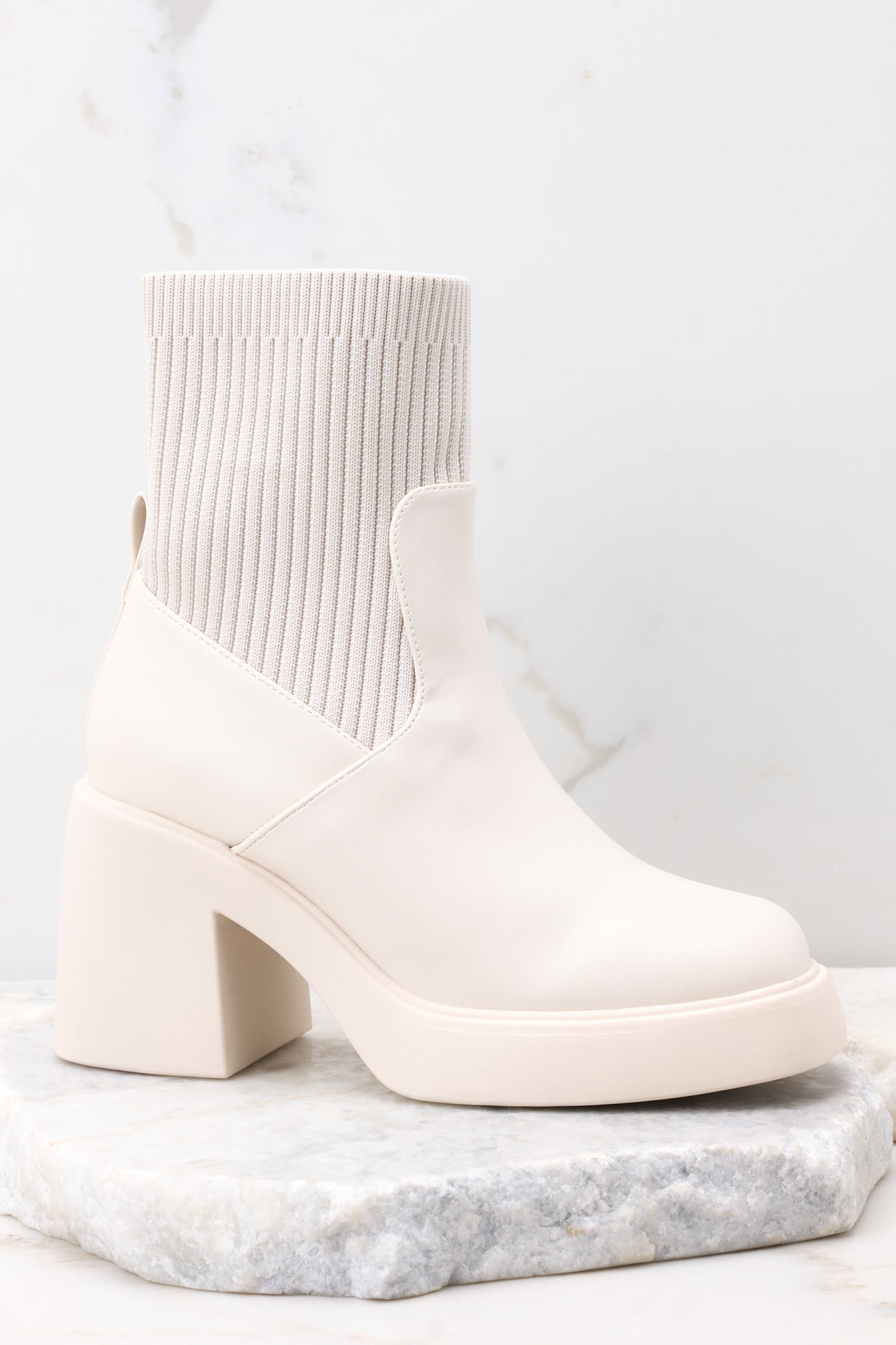 Side view of these boots featuring a rounded toe, a platform heel, and a stretchy ribbed cloth material around the ankle.