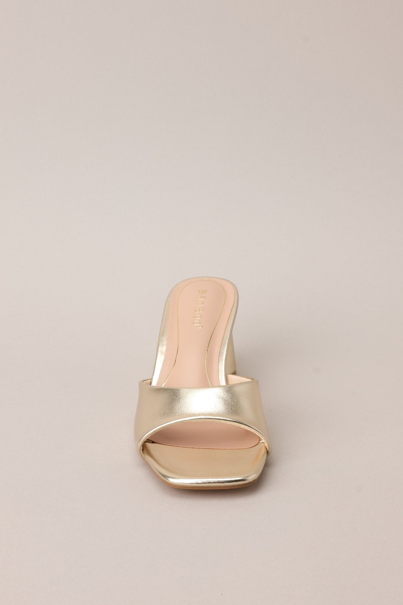 Front view of these gold heels with square toe, slip-on design, strap over foot, short circular heel.