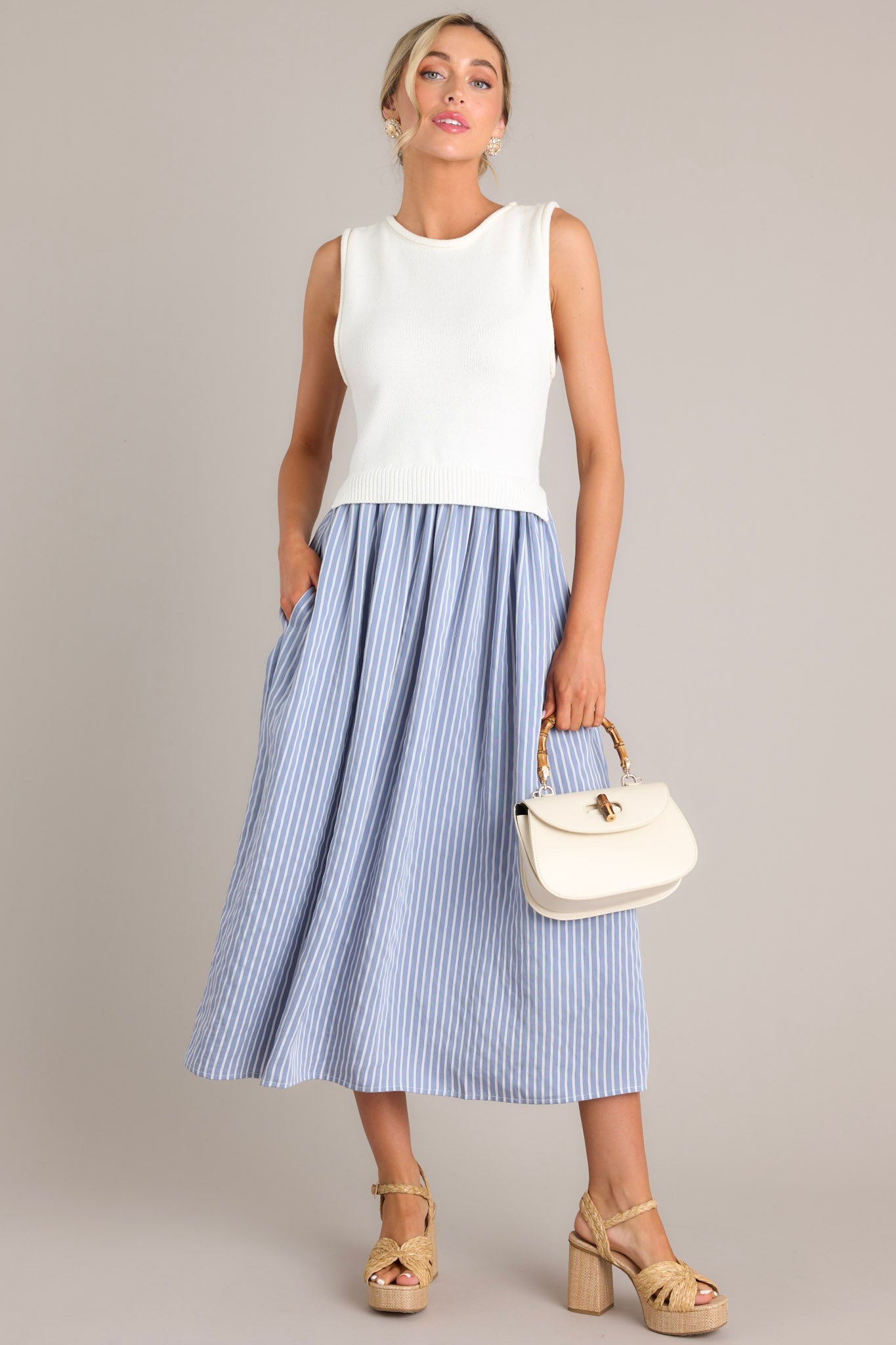 Full length view of a blue striped dress with a high neck design, a knit sleeveless bodice, functional pockets, and a single tiered flowy skirt