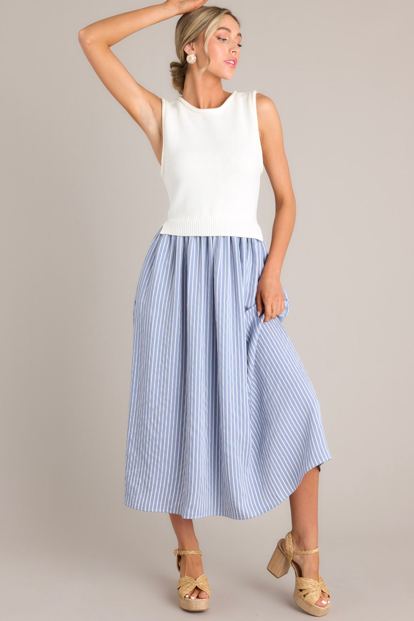 Action shot of a blue striped dress displaying the fit and movement, highlighting the high neck design, knit sleeveless bodice, functional pockets, and single tiered flowy skirt.