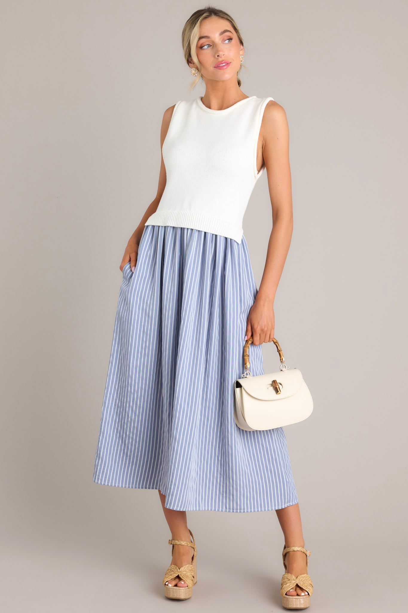 This blue striped dress features a high neck design, a knit sleeveless bodice, functional pockets, and a single tiered flowy skirt