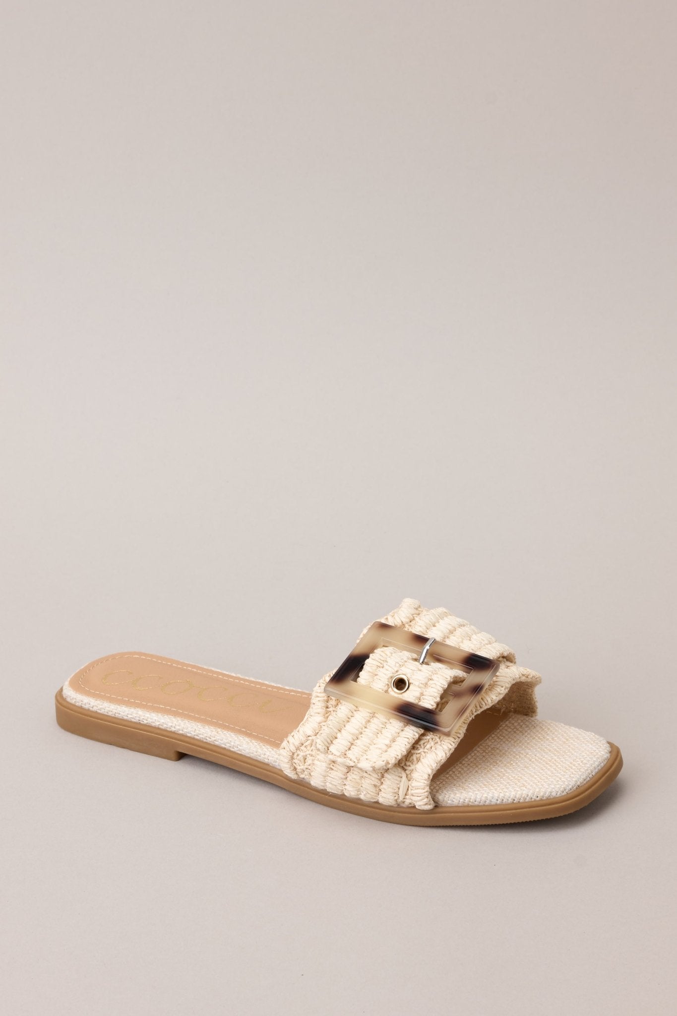 Angled view of these sandals that feature a square toe, a slip-on design, a strap across the top of the foot, a functional buckle, and a woven textured material.