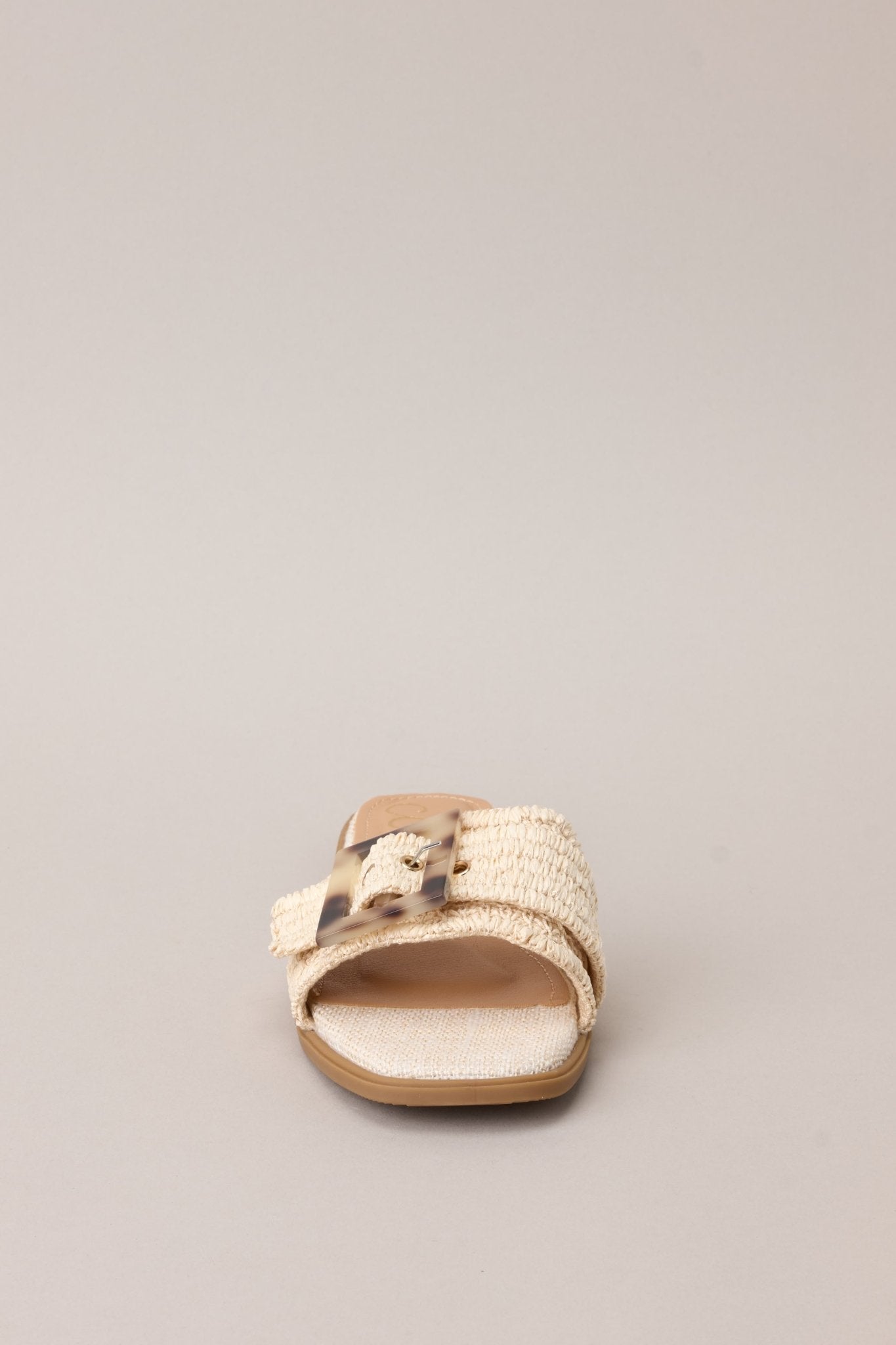 Front view of these sandals that feature a square toe, a slip-on design, a strap across the top of the foot, a functional buckle, and a woven textured material.