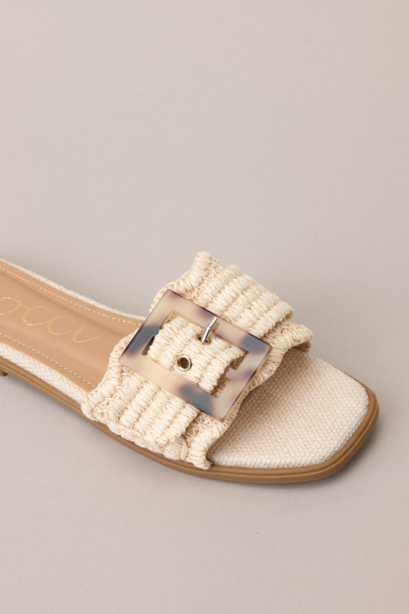 Close-up view of these sandals that feature a square toe, a slip-on design, a strap across the top of the foot, a functional buckle, and a woven textured material.