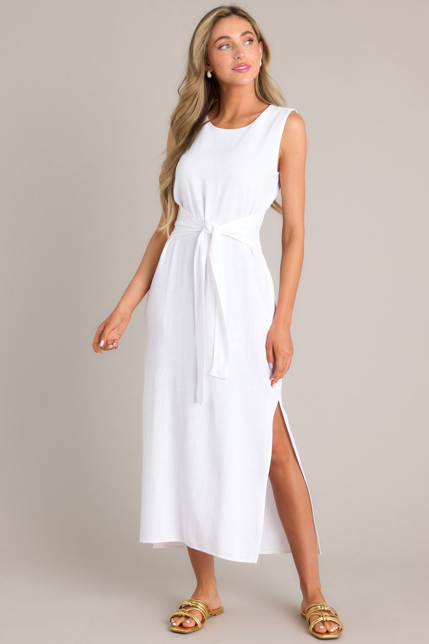 This white dress features a rounded neckline, a back keyhole cutout with functional button, a smocked back insert, a self-tie waist feature, functional hip pockets, and side slits.