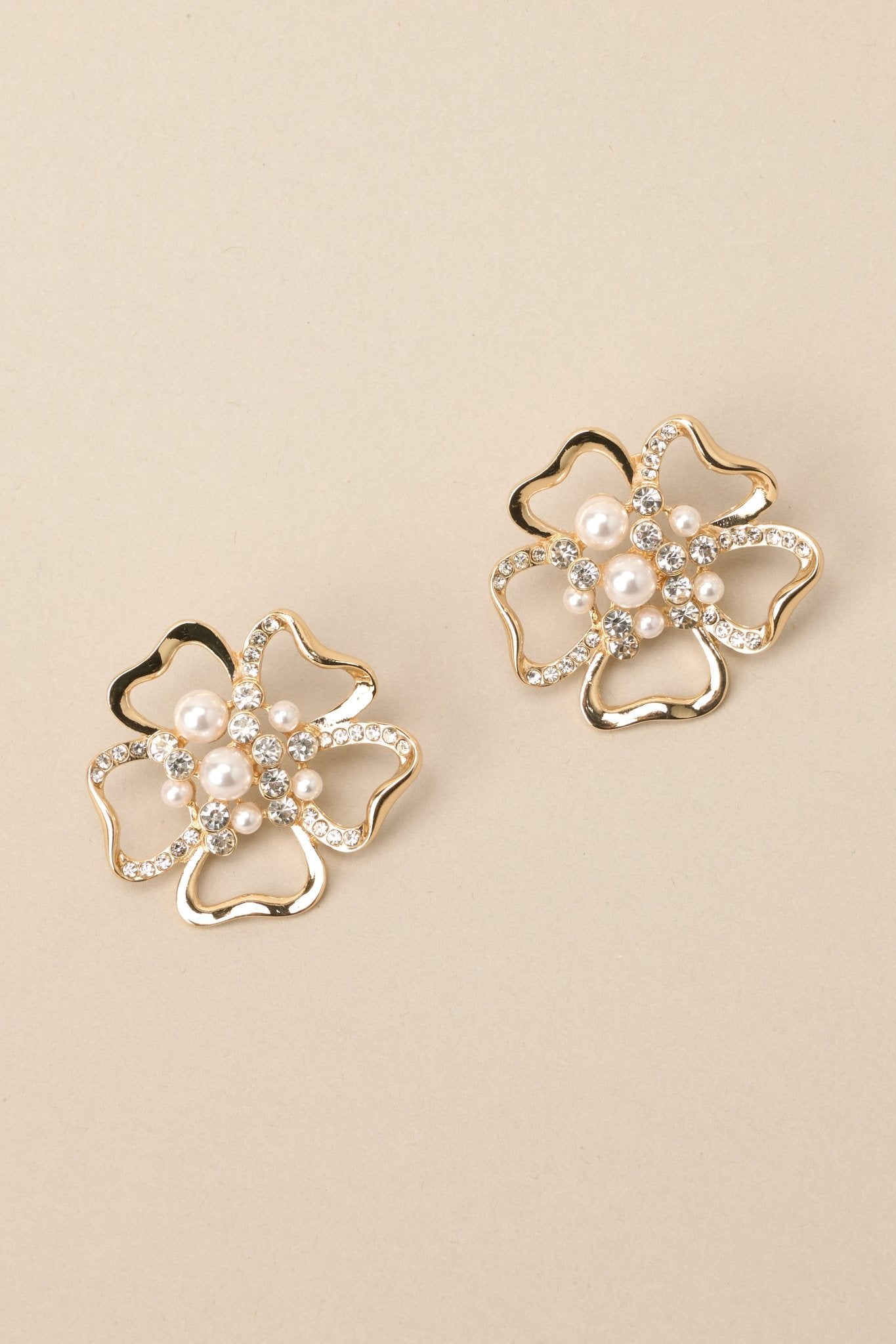 Earrings featuring a flower shape embellished with faux pearls and rhinestones, and secure post backings on a solid backdrop. 