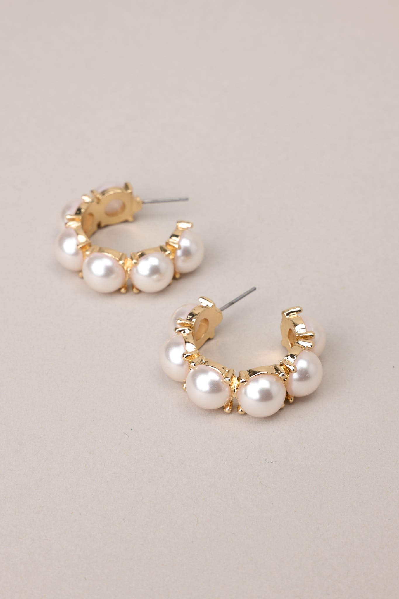 Side view of  these pearl hoop earrings that feature gold hardware, six hemisphere pearls along the hoop, and a secure post backing.