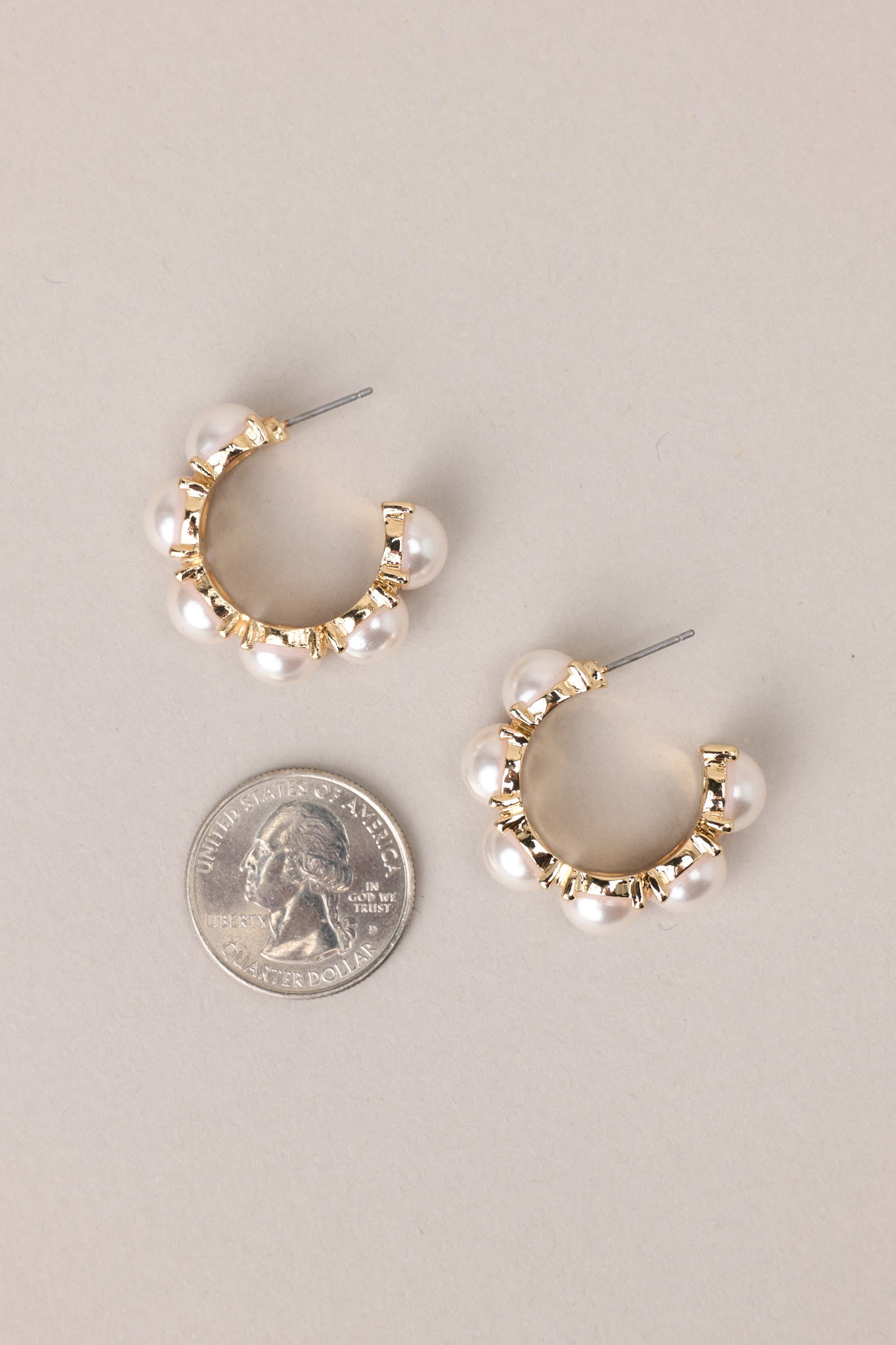 Size comparison of these pearl hoop earrings that feature gold hardware, six hemisphere pearls along the hoop, and a secure post backing.