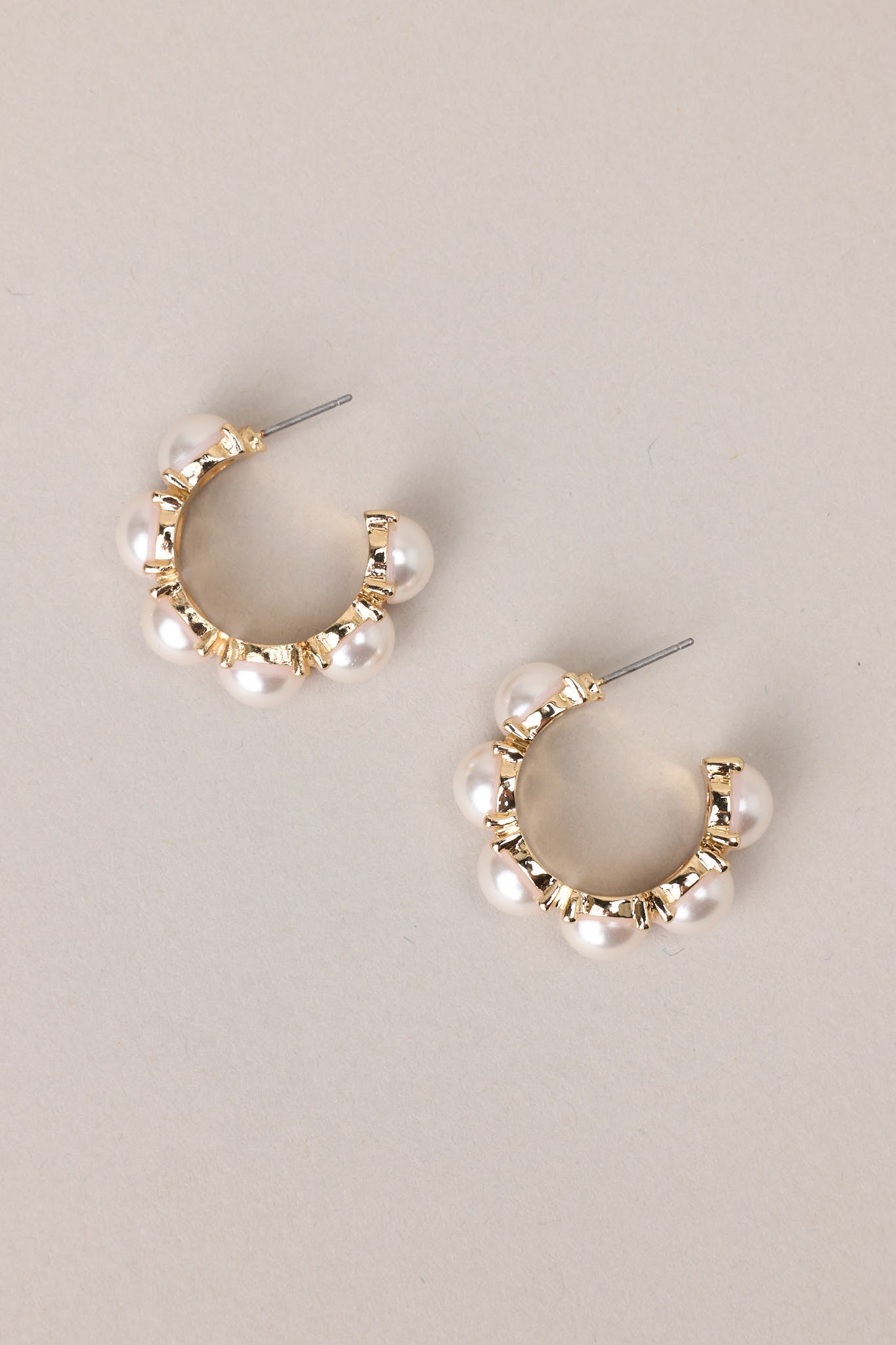 Top view of these pearl hoop earrings that feature gold hardware, six hemisphere pearls along the hoop, and a secure post backing.