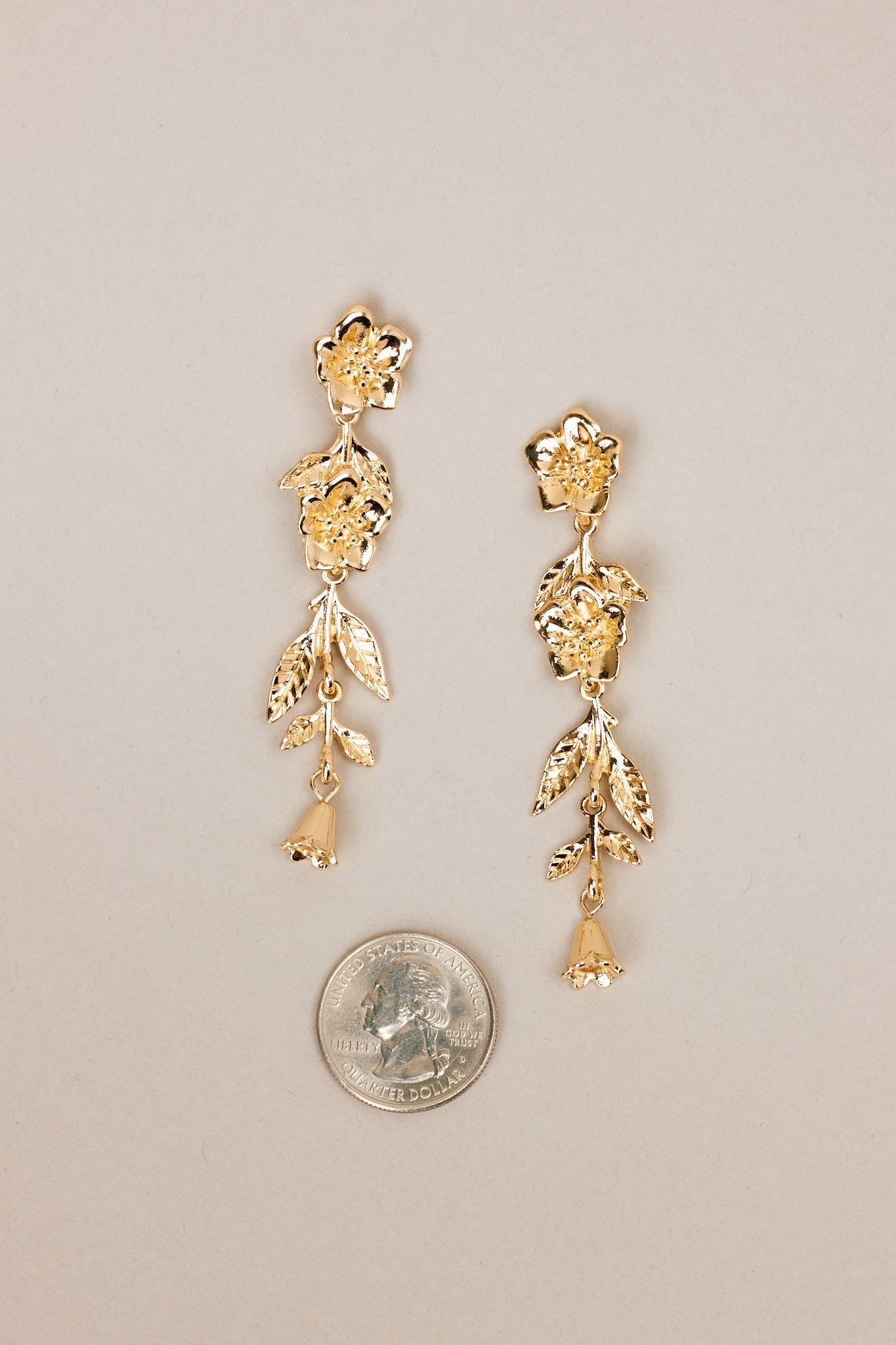 Size comparison of these gold floral earrings that feature gold hardware, a flower shaped stud, and secure post backings.