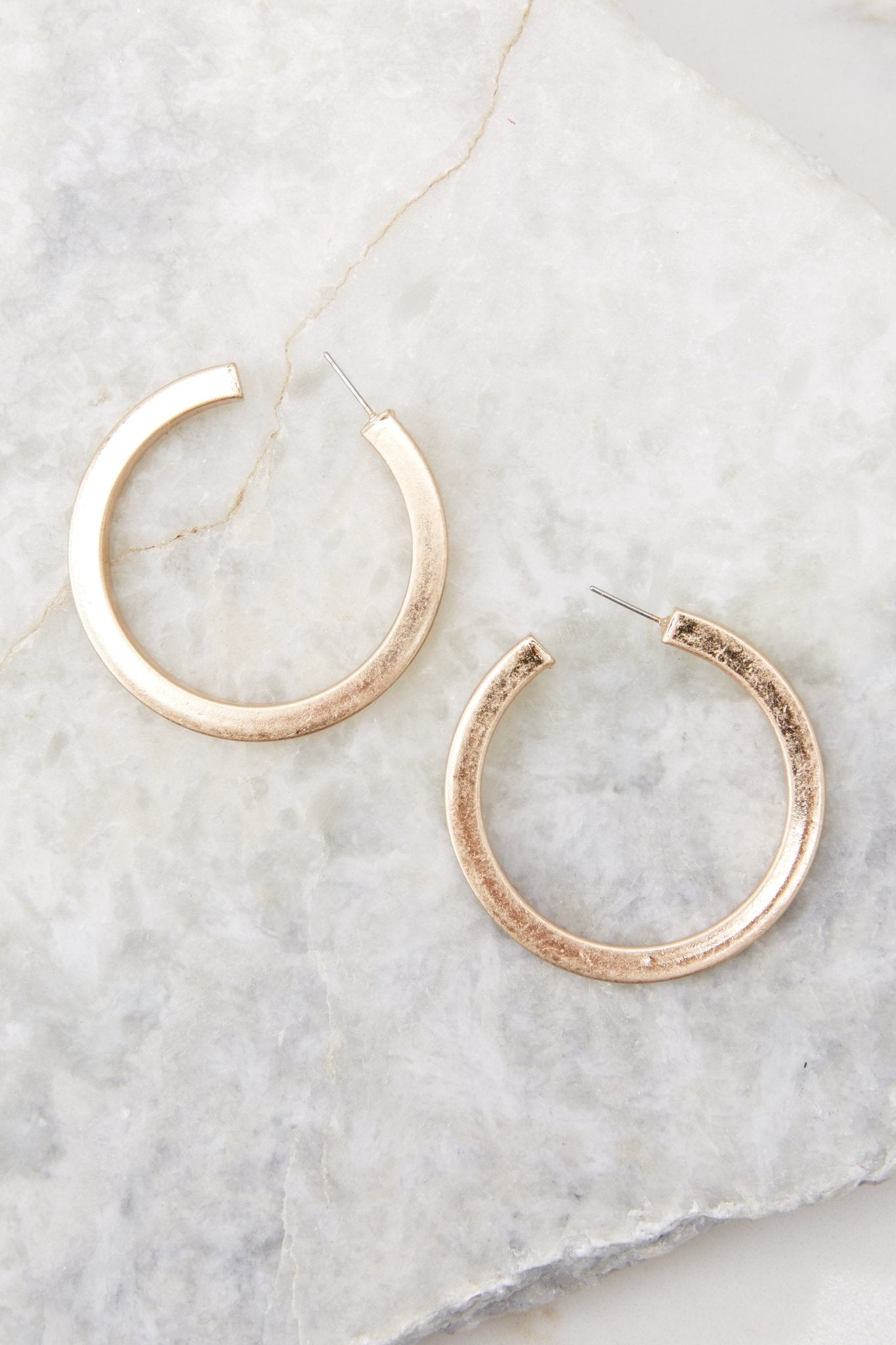 Overhead close up view of chunky gold hoop earrings with a standard post back fastening. 