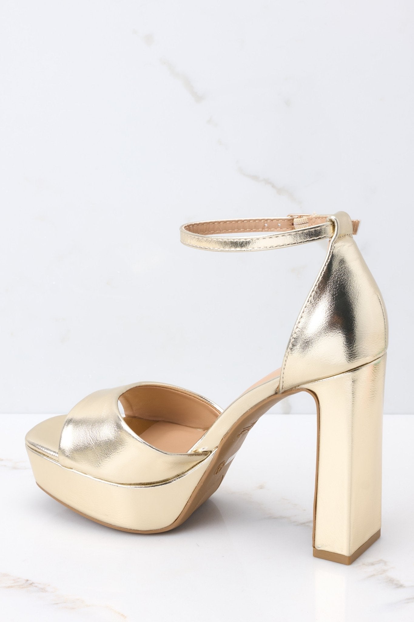 Inner-side view of  these shoes that feature an adjustable ankle strap, a gold strap over the foot, a chucky heel, and a platform style.